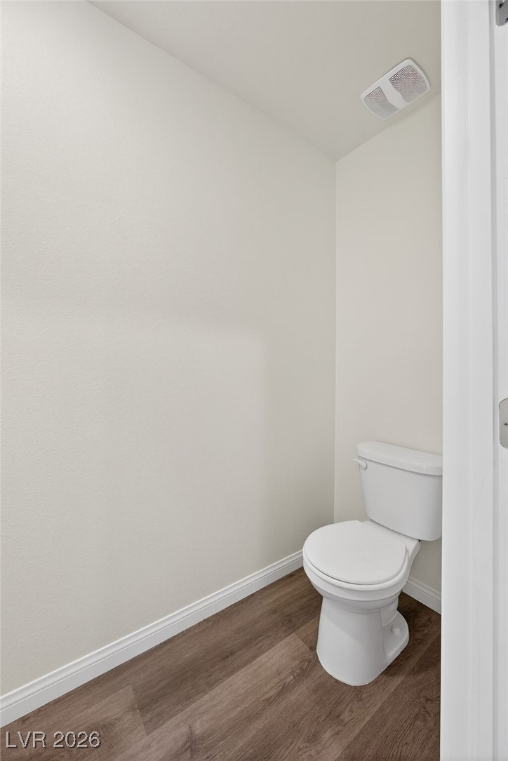 Small bathroom with a white toilet and brown wood-look flooring.