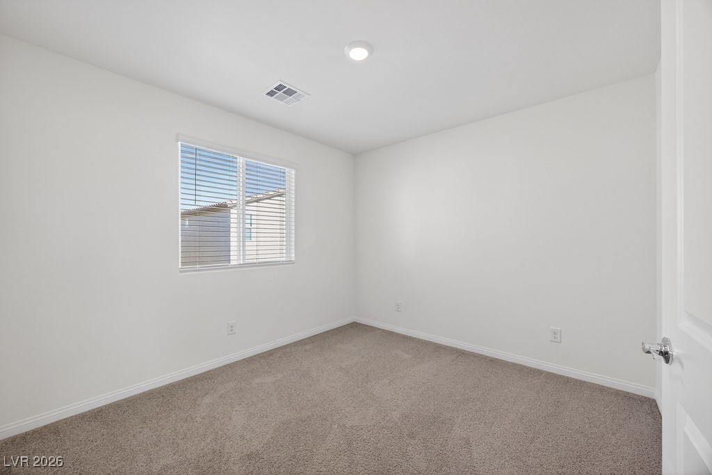 Empty carpeted bedroom with a window fitted with white blinds.