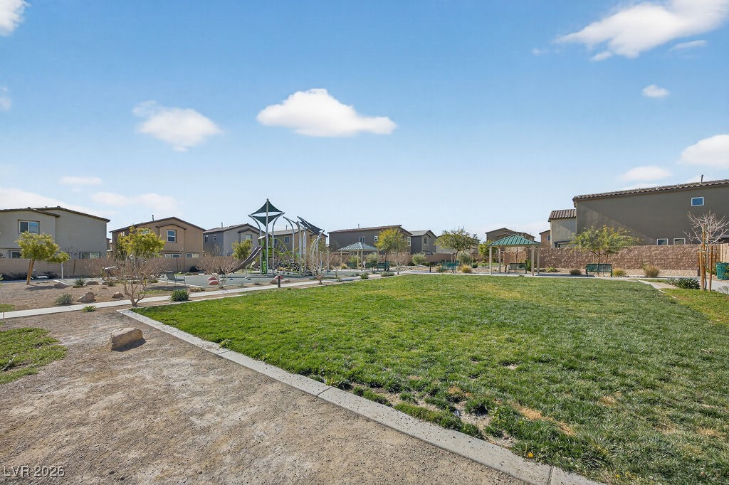 Neighborhood park with a grassy lawn, playground slides, and homes in the background.
