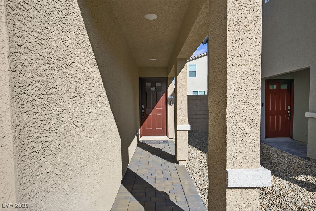 Covered stucco entry with red front door, paver walkway, and gravel landscaping.