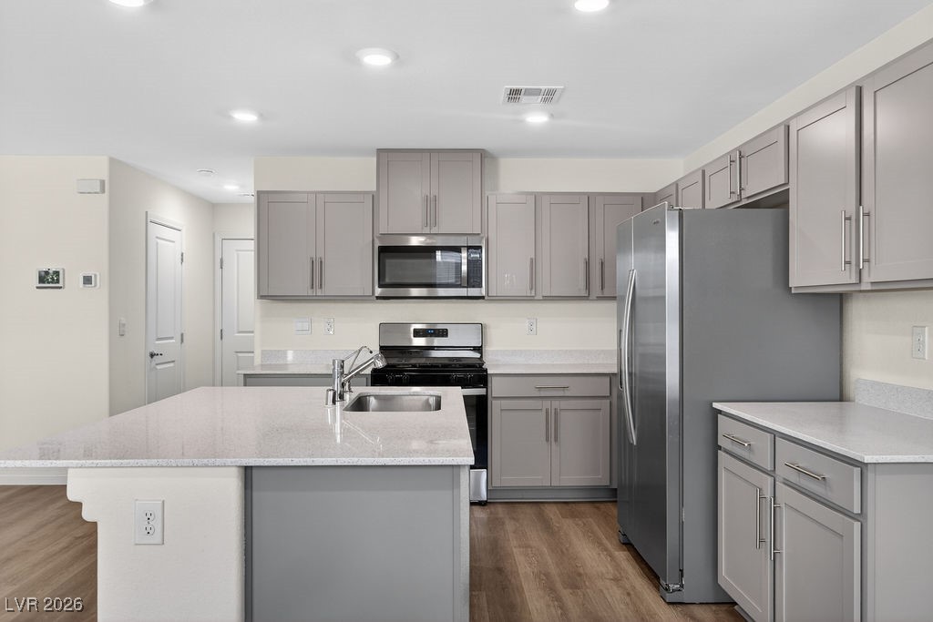 Kitchen with gray cabinets, quartz island, stainless steel appliances, and wood-look flooring.