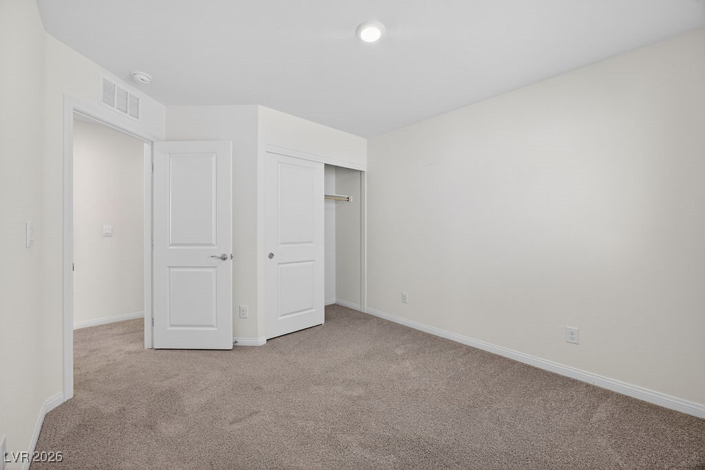 Empty bedroom with beige carpet and an open closet.