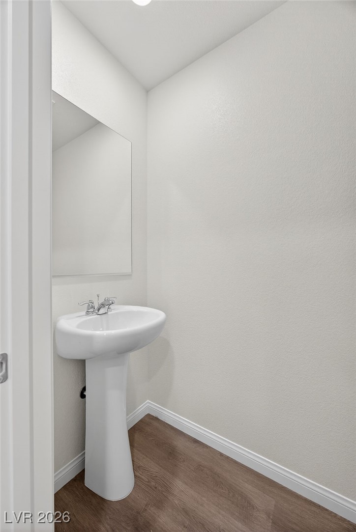Small bathroom with a white pedestal sink, wall mirror, and wood-look flooring.