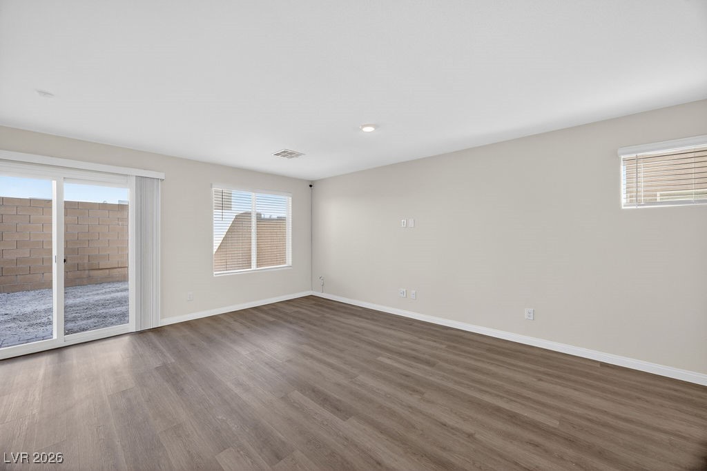 Vacant living room with plank flooring and a sliding glass door to a walled patio.