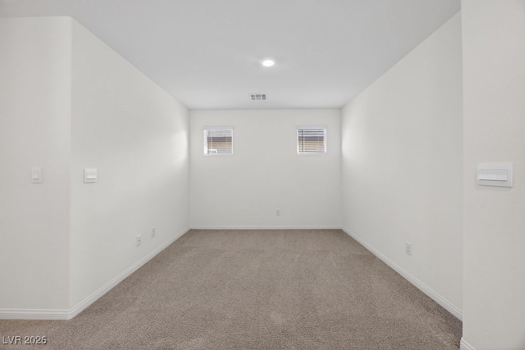 Empty carpeted room with two small windows and a recessed ceiling light.