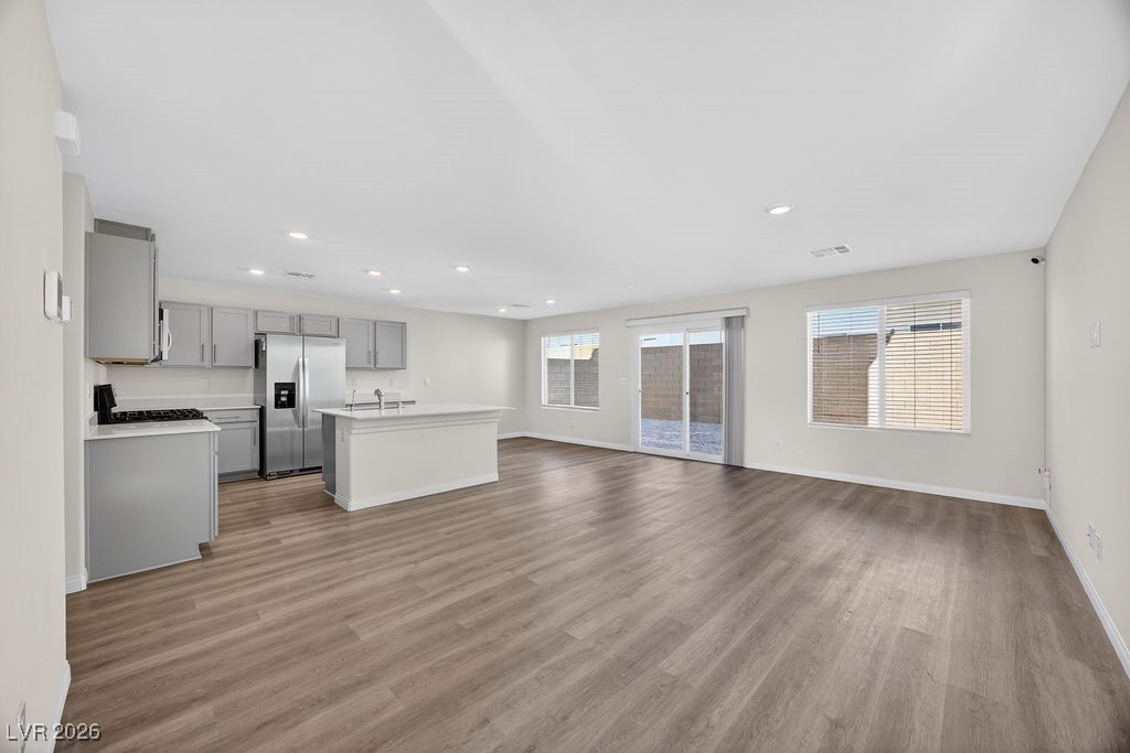 Vacant open-plan kitchen and living area with gray cabinets, a large island, and wood-look flooring.