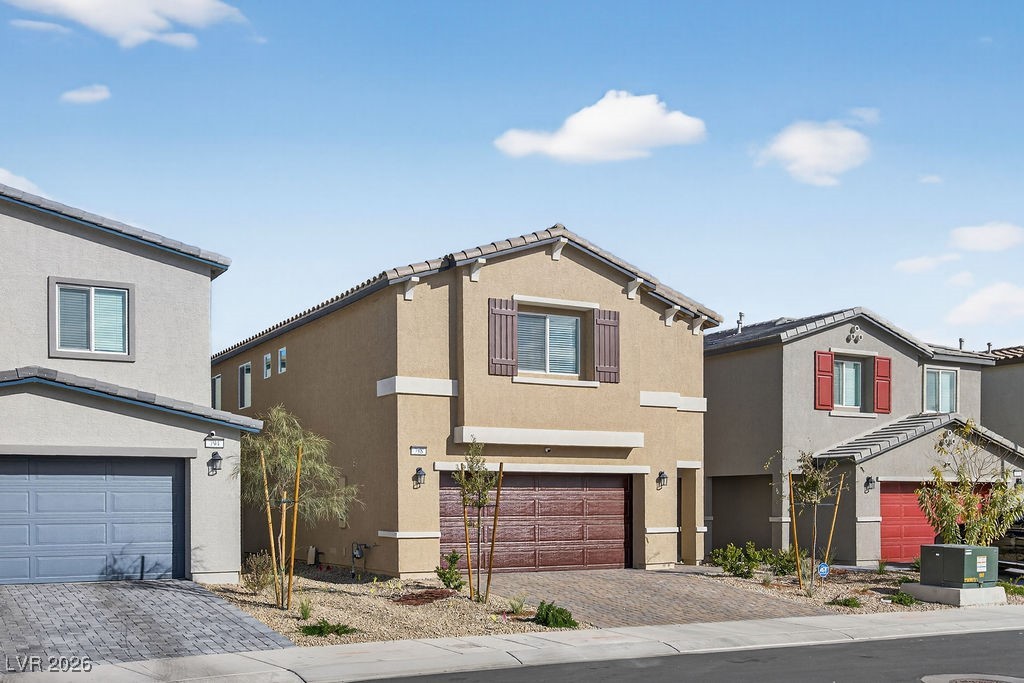 Two-story tan stucco home with brown garage door, decorative shutters, and paver driveway.