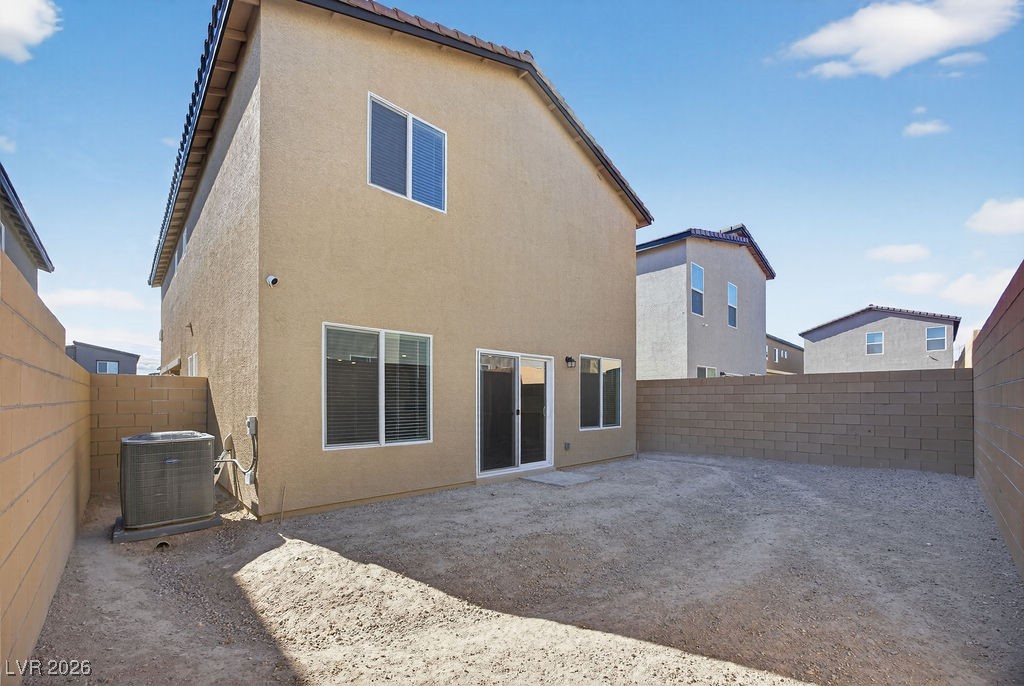 Two-story tan home overlooking an enclosed dirt backyard with block walls and an air-conditioning unit.