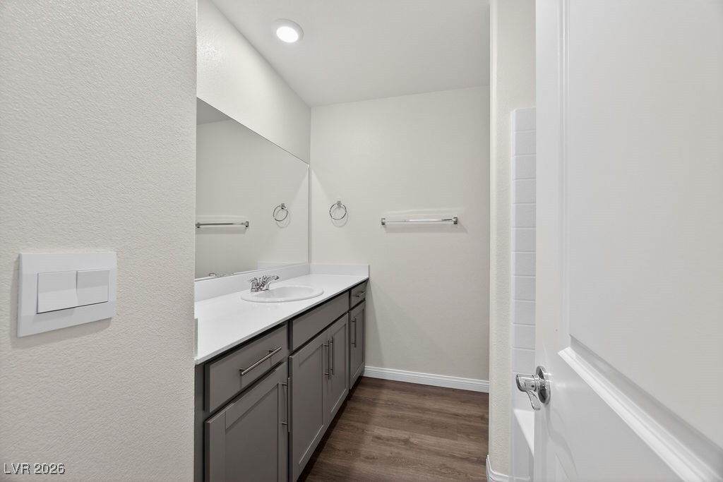 Bathroom with gray vanity, white countertop, large mirror, and wood-look flooring.