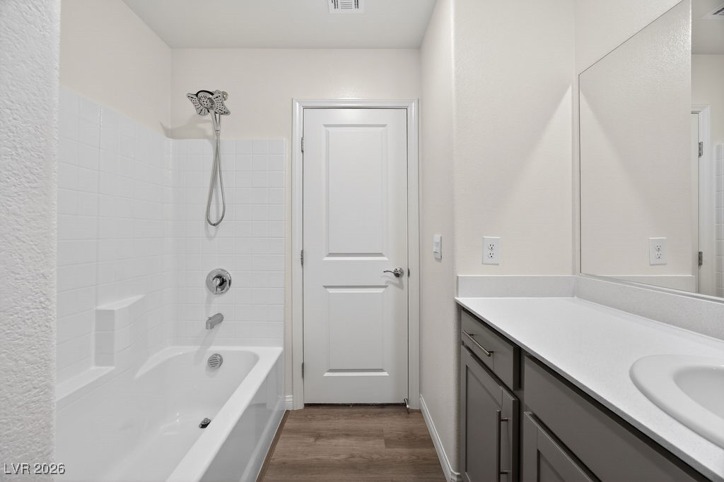 Bathroom with a tiled tub and shower, gray vanity, white countertop, and large mirror.