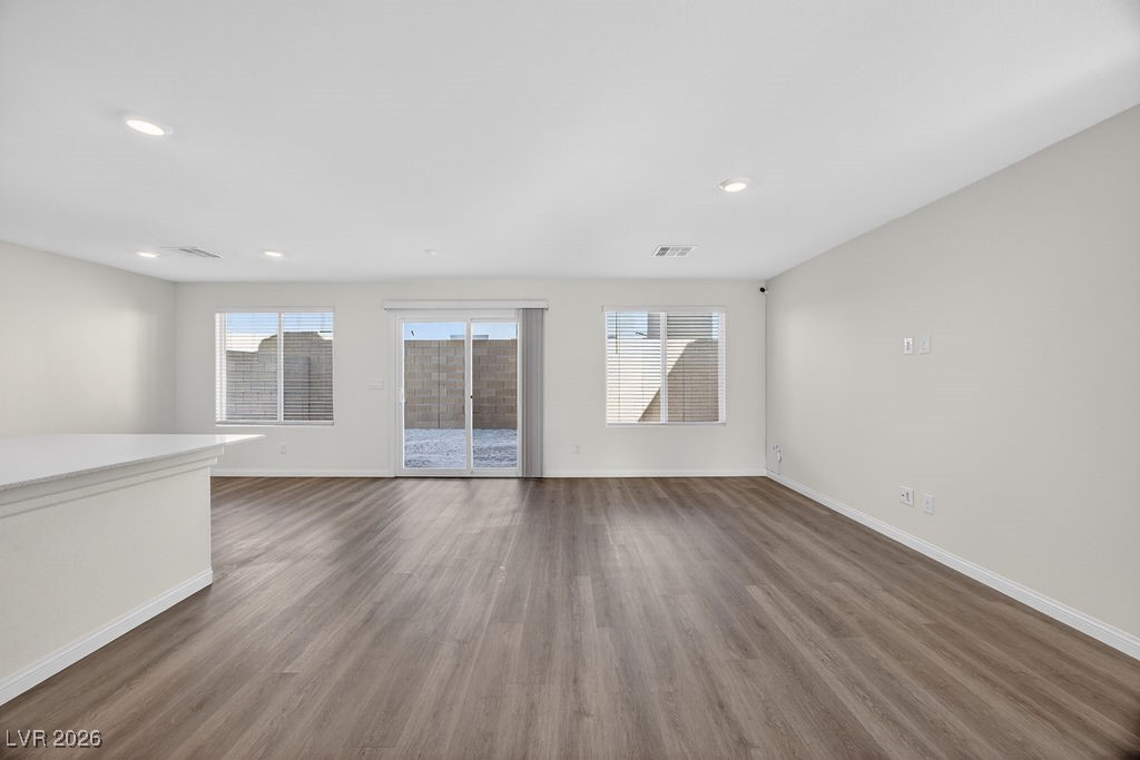 Vacant living room with wood-look flooring, recessed lights, and sliding glass doors.