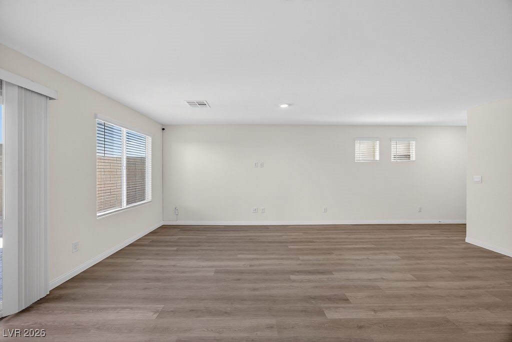 Empty living room with wide-plank flooring, large windows, and vertical blinds by a sliding glass door.