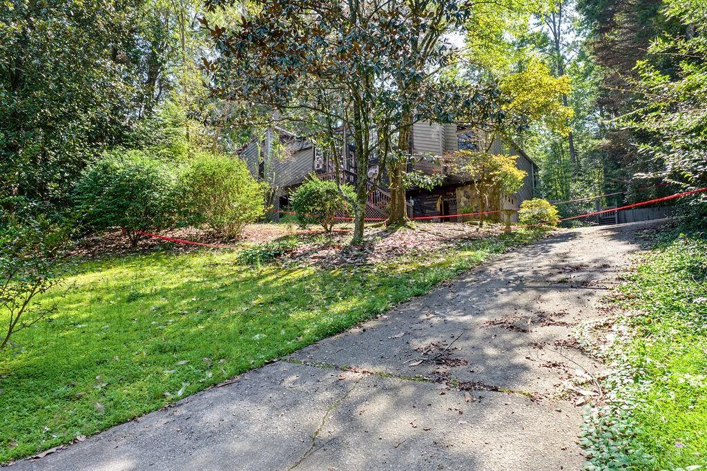 Gray house among mature trees, with a raised deck and sloped driveway.