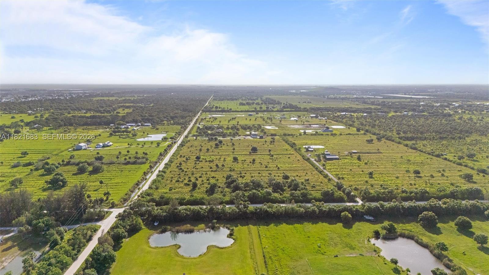 Aerial view of green rural fields with farm buildings, a straight road, and two ponds.