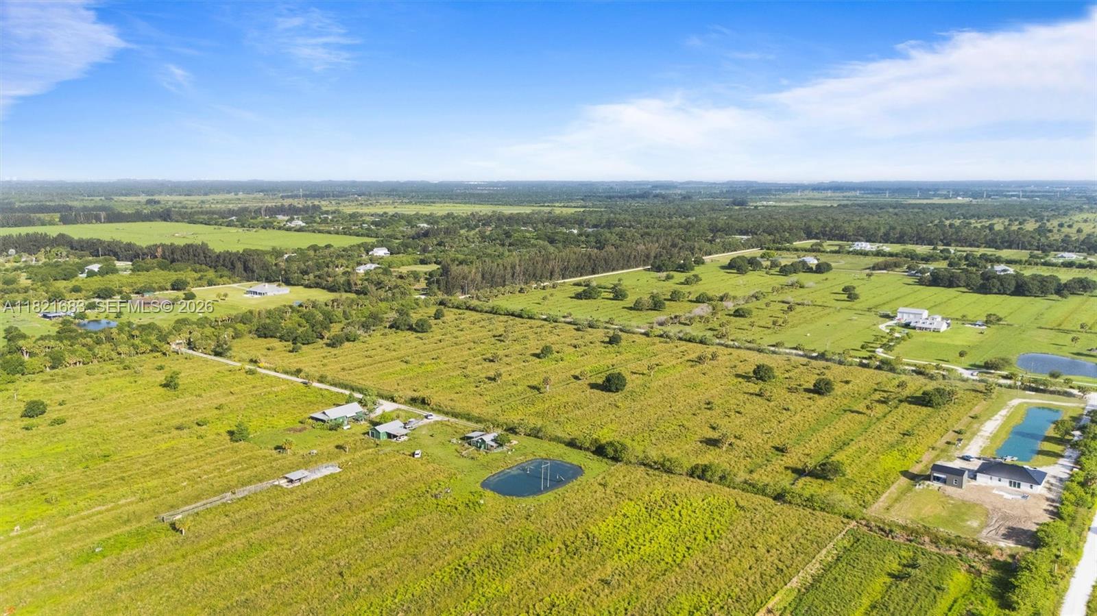 Aerial view of green rural fields with scattered homes and small ponds.