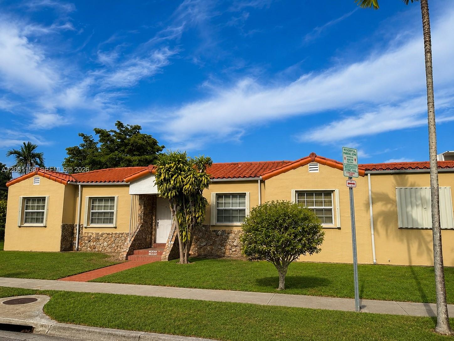 Yellow single-story house with a red tile roof, stone entry accents, and tropical landscaping.