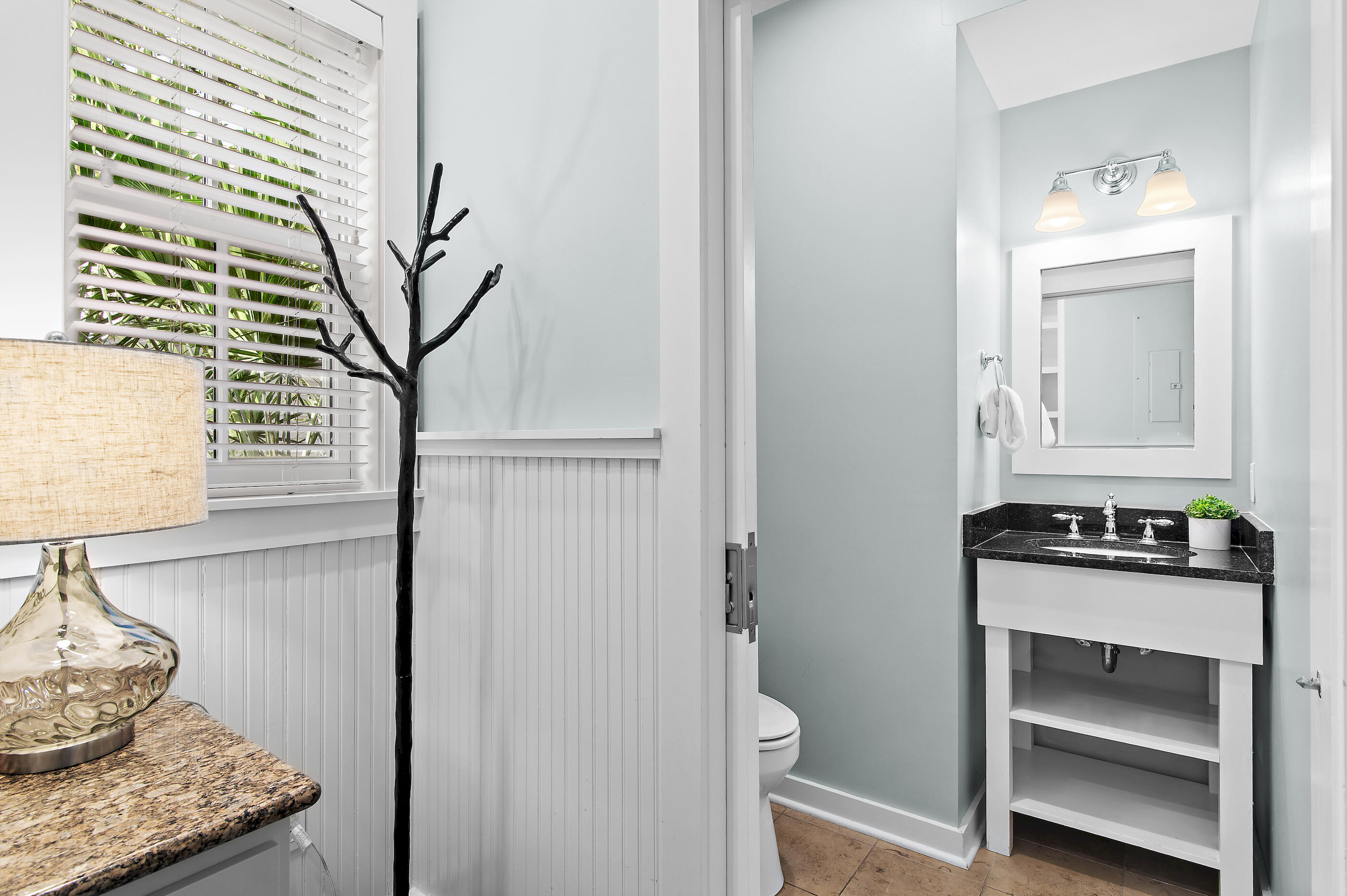 Bathroom with a black stone vanity, framed mirror, and window overlooking greenery.