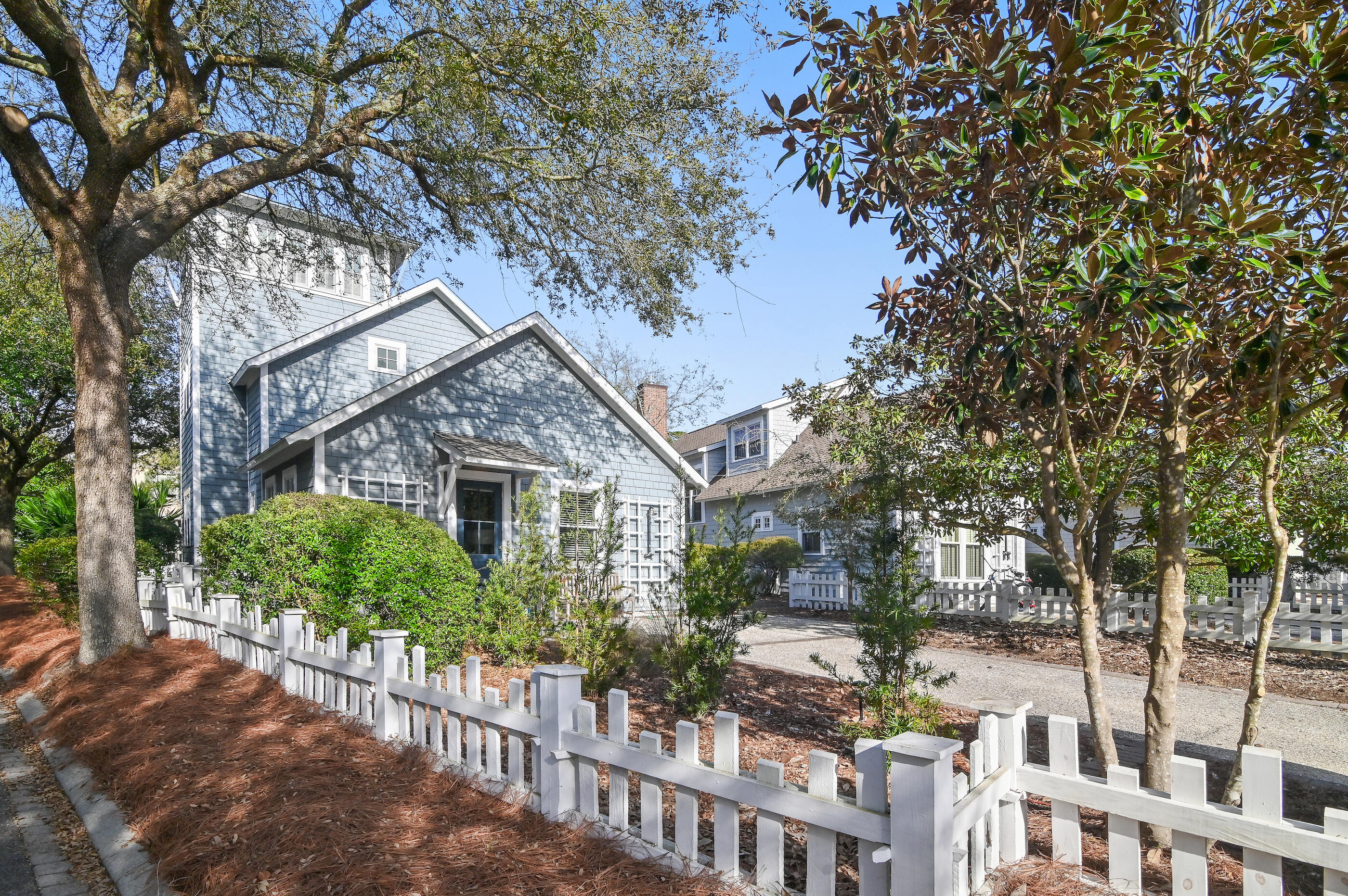 Blue-shingled home behind a white picket fence, framed by mature trees.