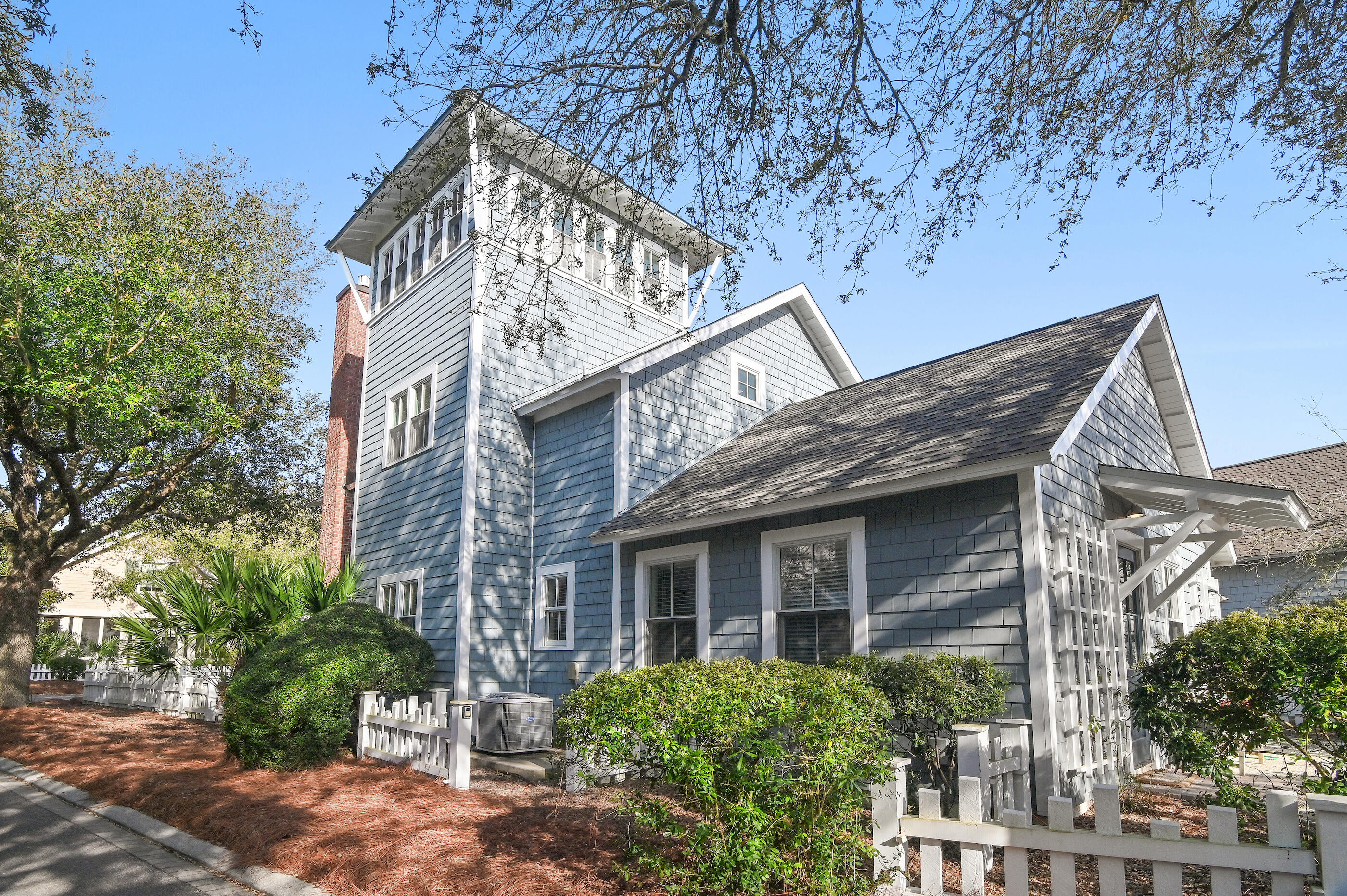 Blue shingle-sided coastal house with a tower, brick chimney, and white picket fence.