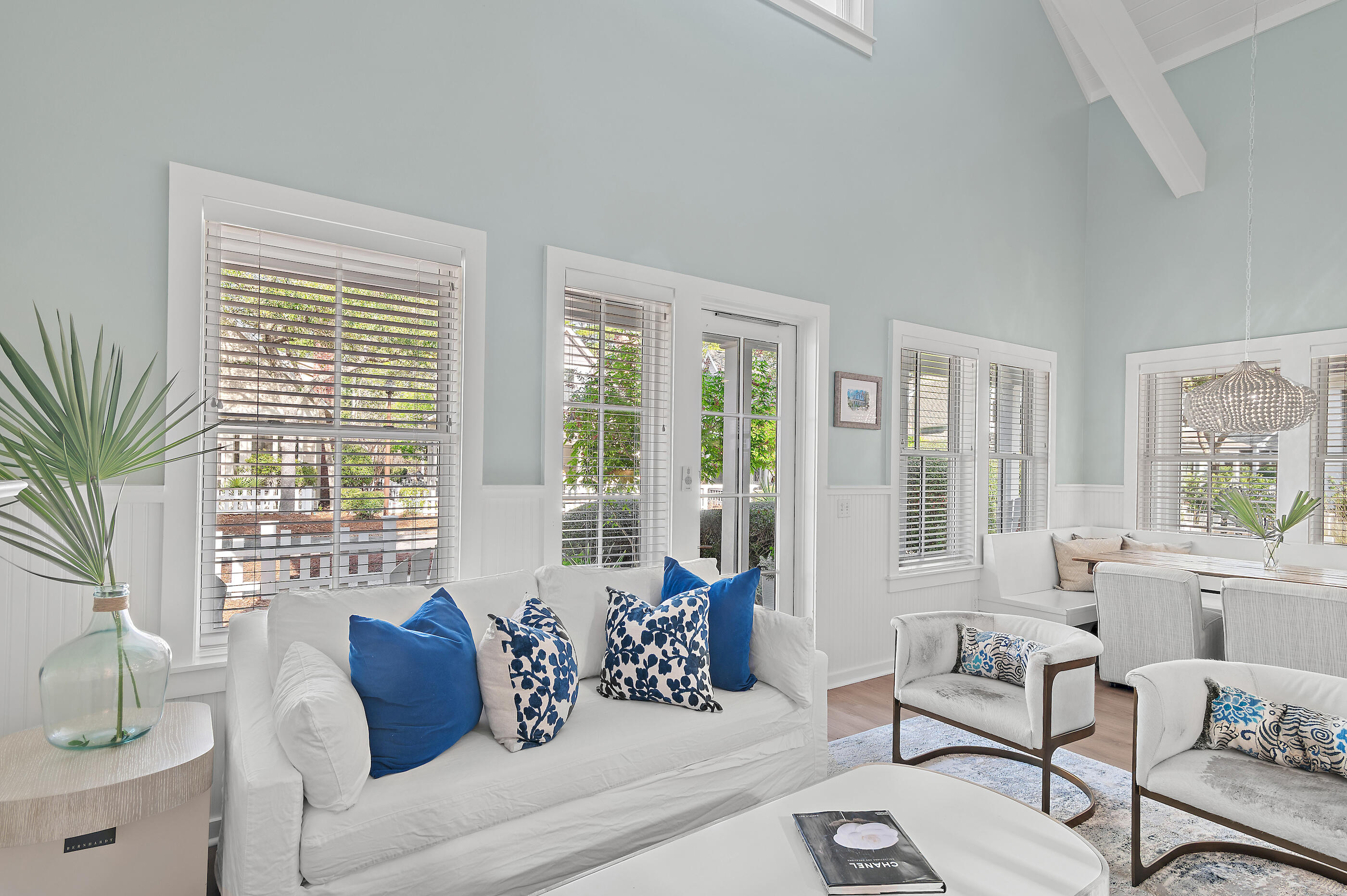 Bright living room with white seating, blue accent pillows, and large shuttered windows.
