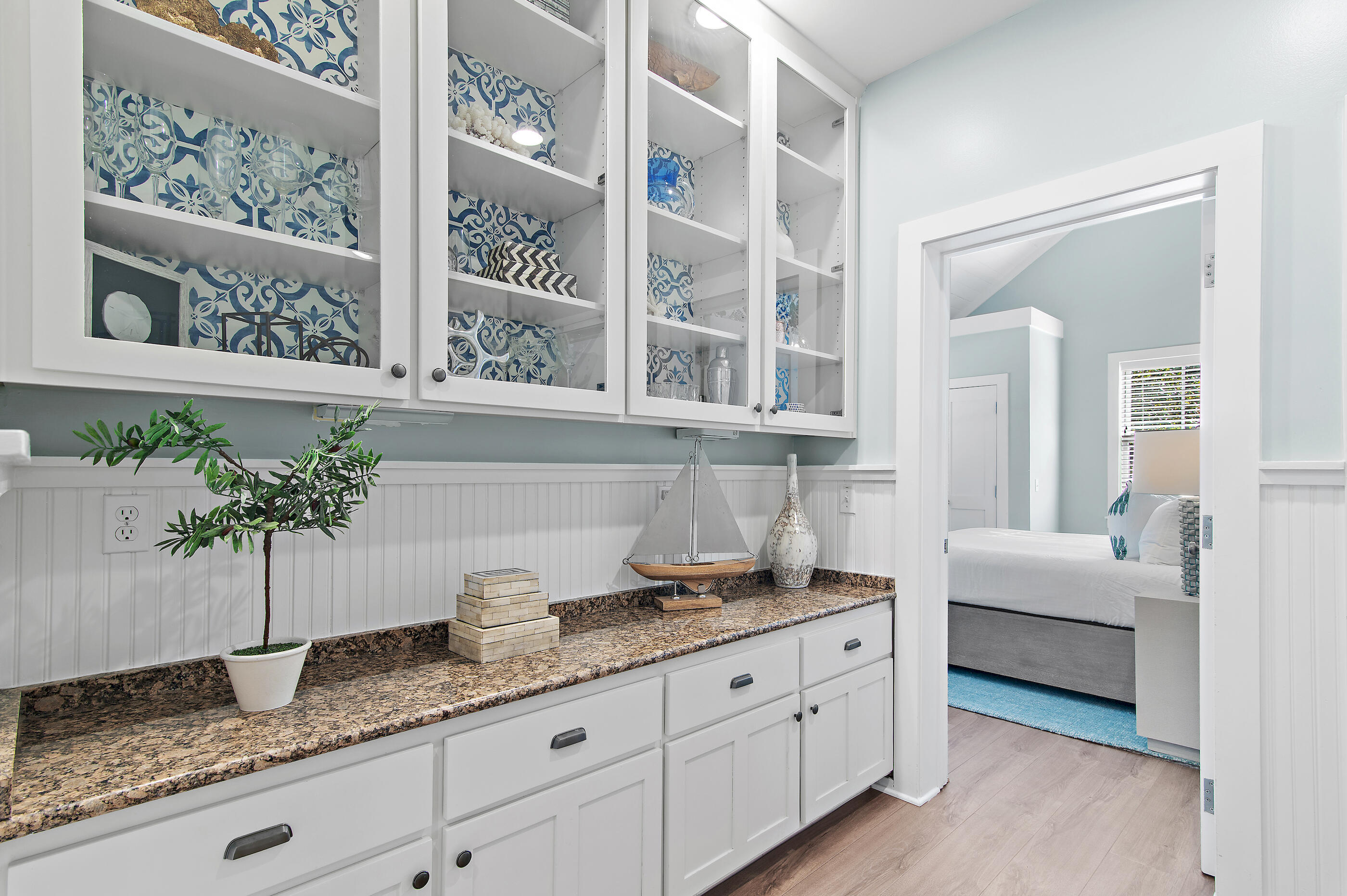 Built-in serving area with glass-front cabinets, blue patterned tile, granite counter, and bedroom doorway.