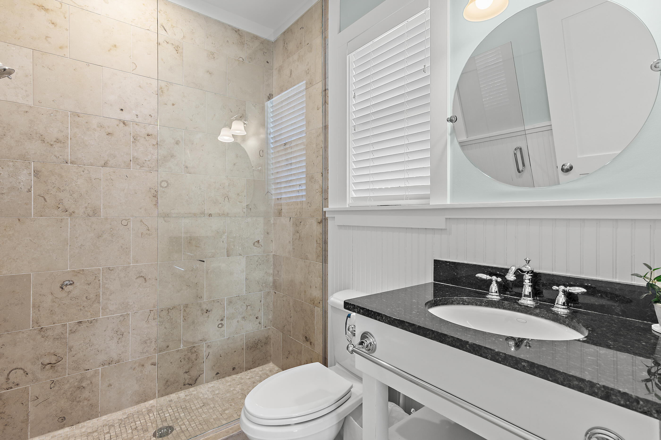 Bathroom with a stone-tile walk-in shower and a white vanity with black countertop.