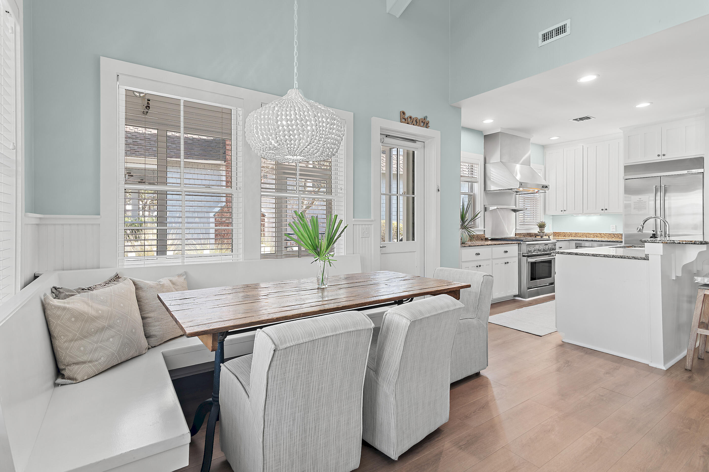 Dining area with a wood table, built-in bench, sculptural pendant, and open white kitchen.