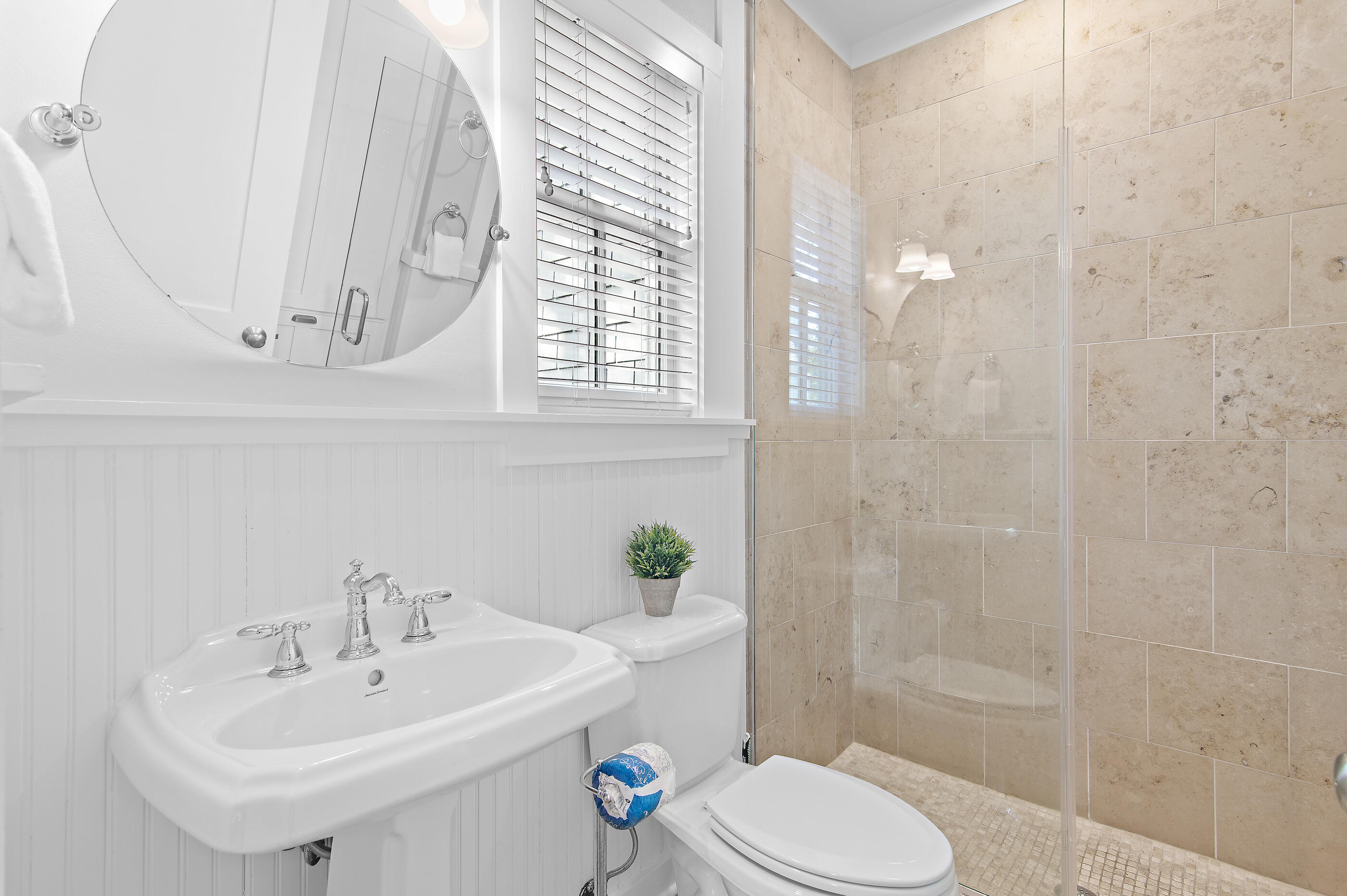 Bathroom with a white pedestal sink and toilet beside a beige-tiled glass shower.