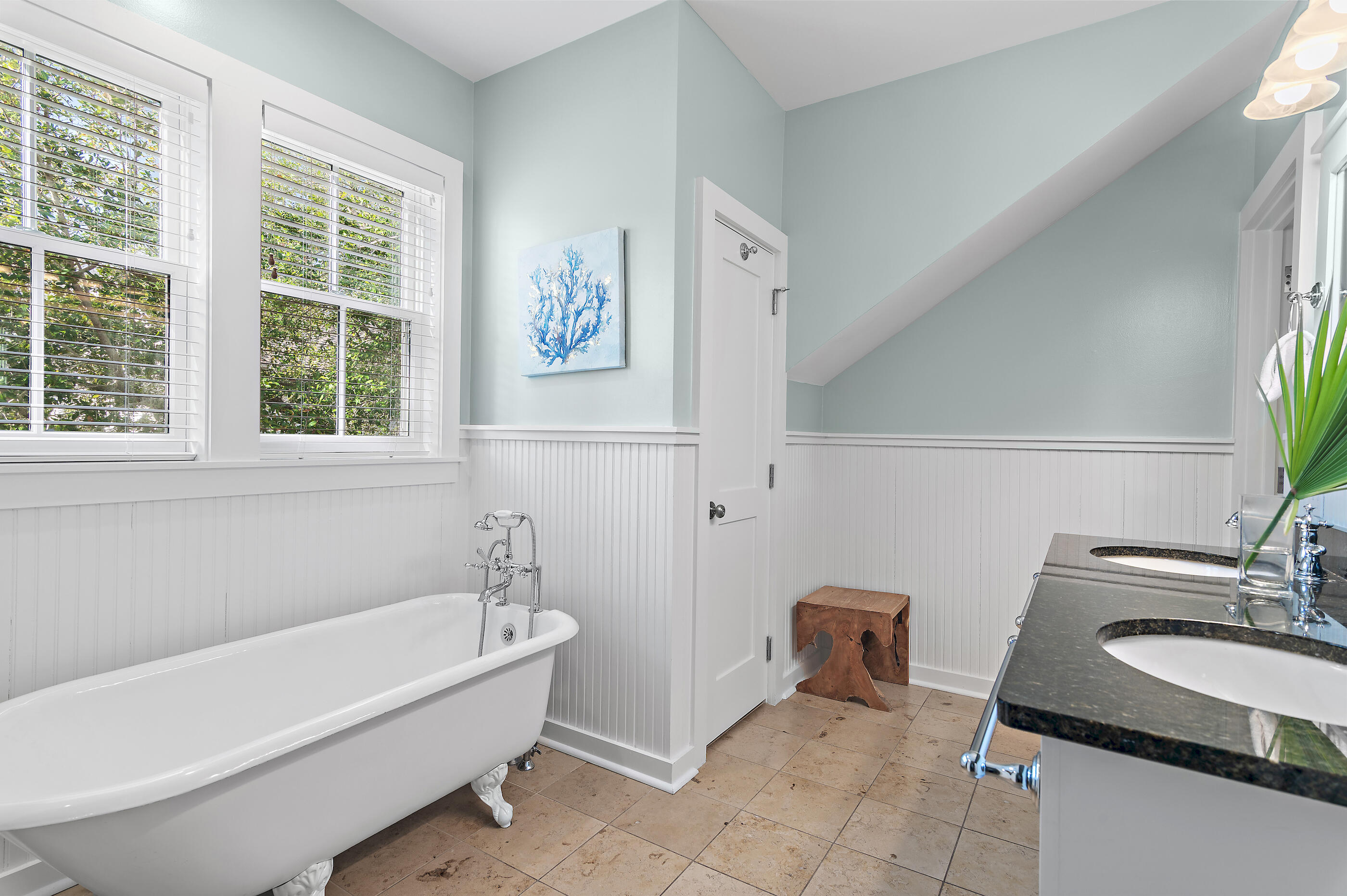Bright bathroom with a clawfoot tub, dark double-sink vanity, and blue coral artwork.