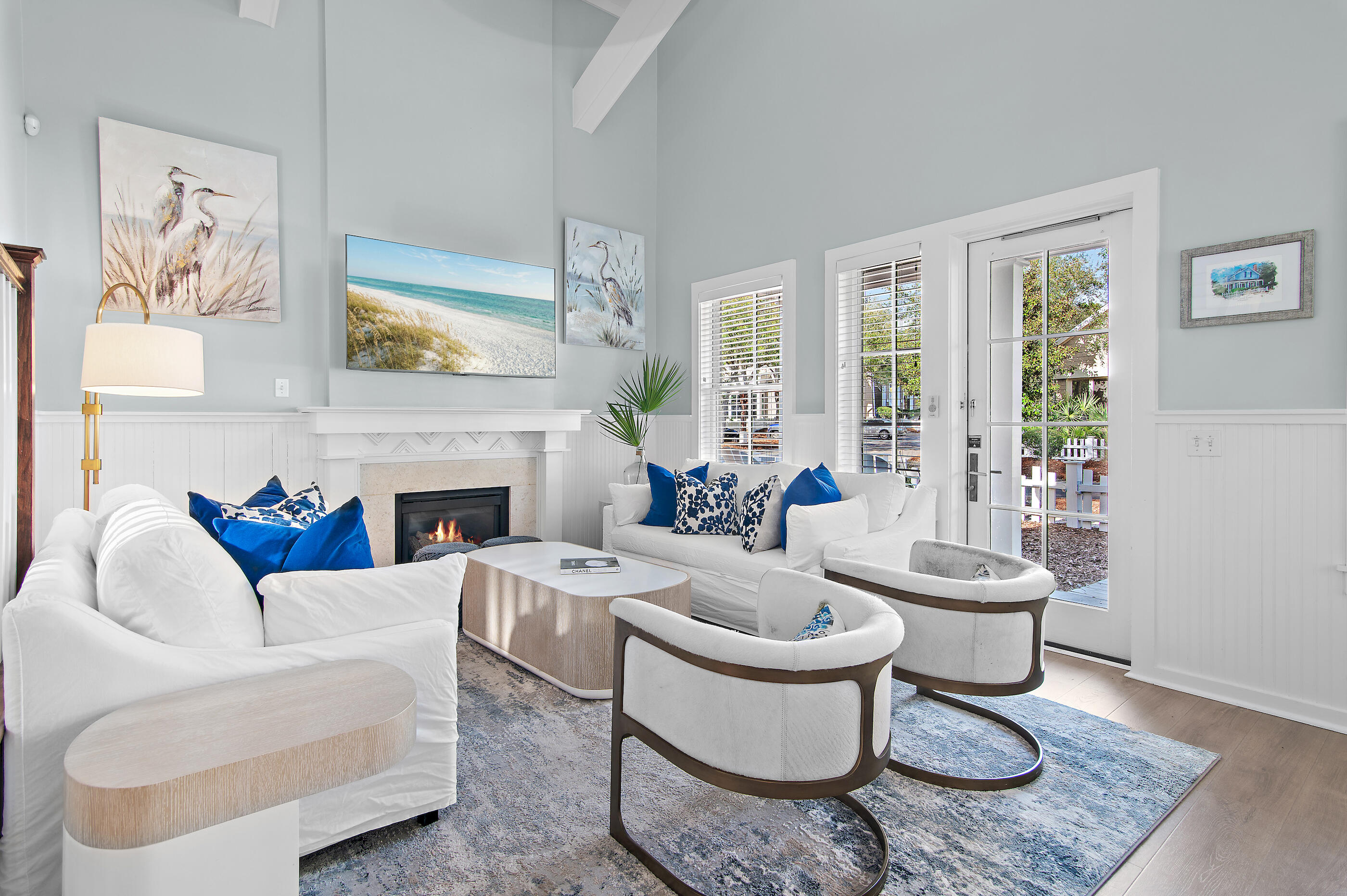 Furnished living room with white seating, blue accents, a lit fireplace, and a glass-paneled door.