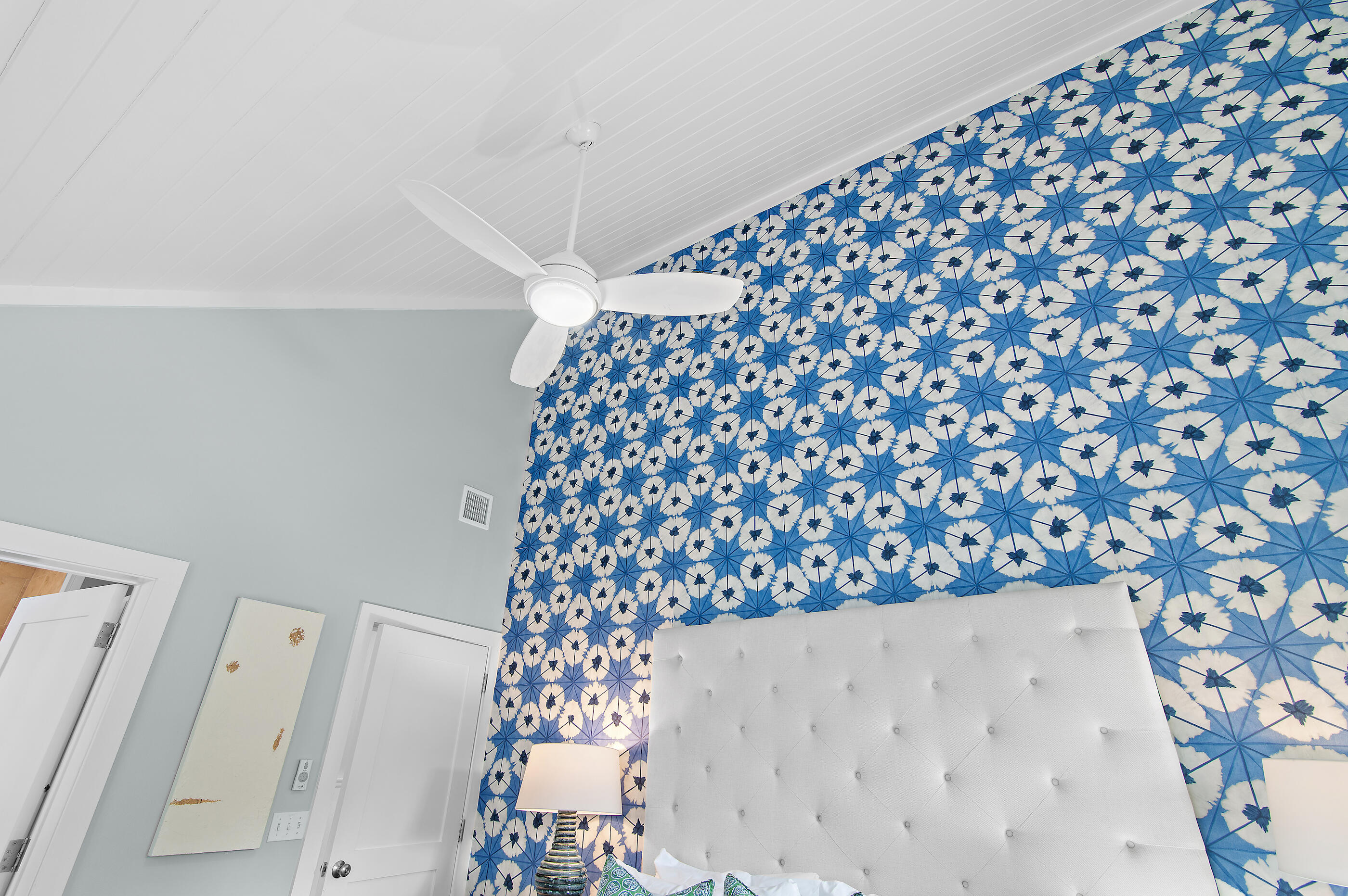 Bedroom with a blue-and-white patterned accent wall, white tufted headboard, and vaulted ceiling fan.