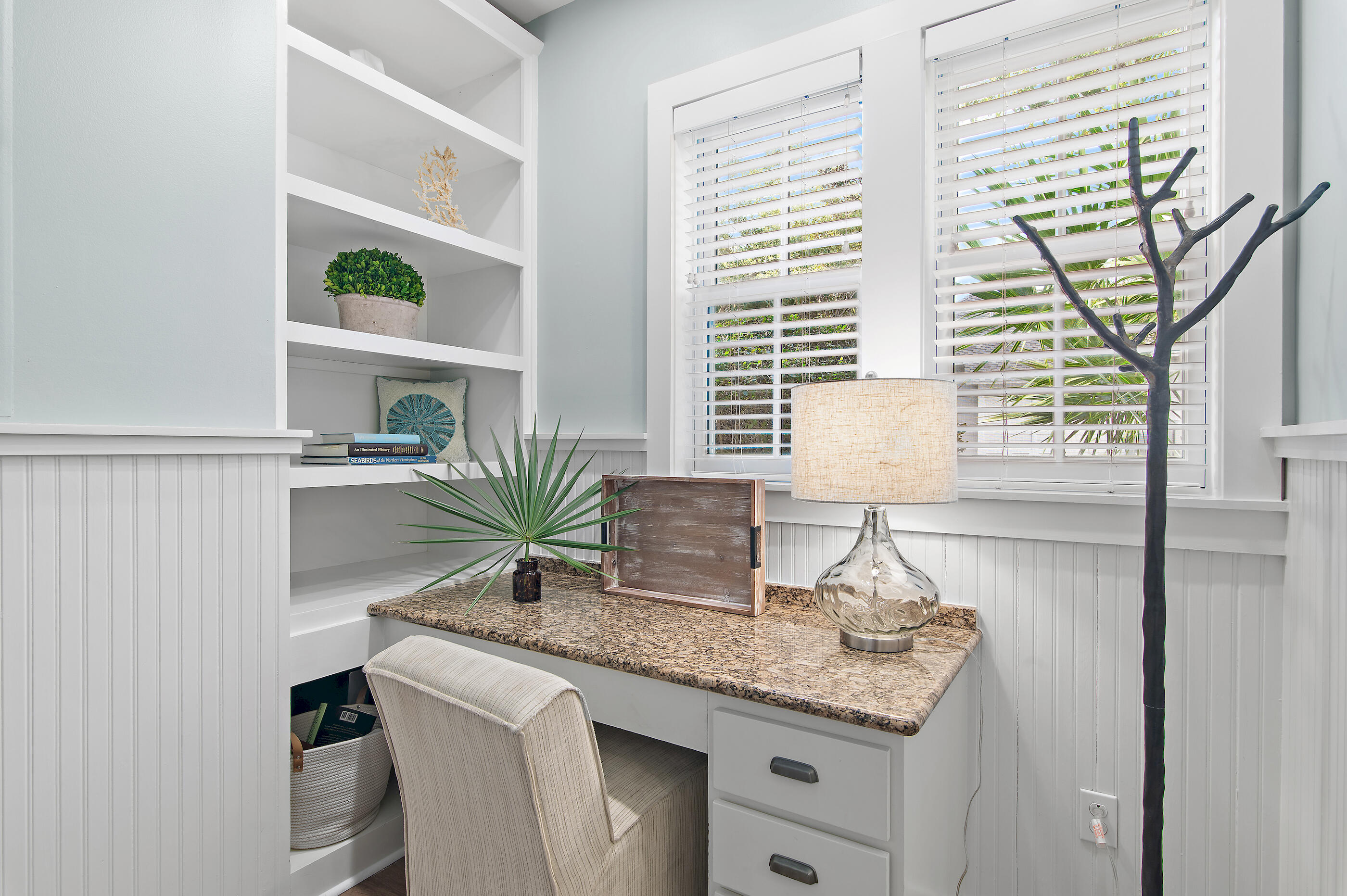Home office nook with a granite desk, built-in shelves, and windows overlooking greenery.