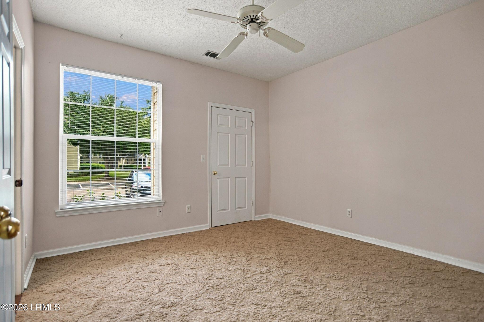 Empty carpeted bedroom with a ceiling fan, window blinds, and a paneled door.