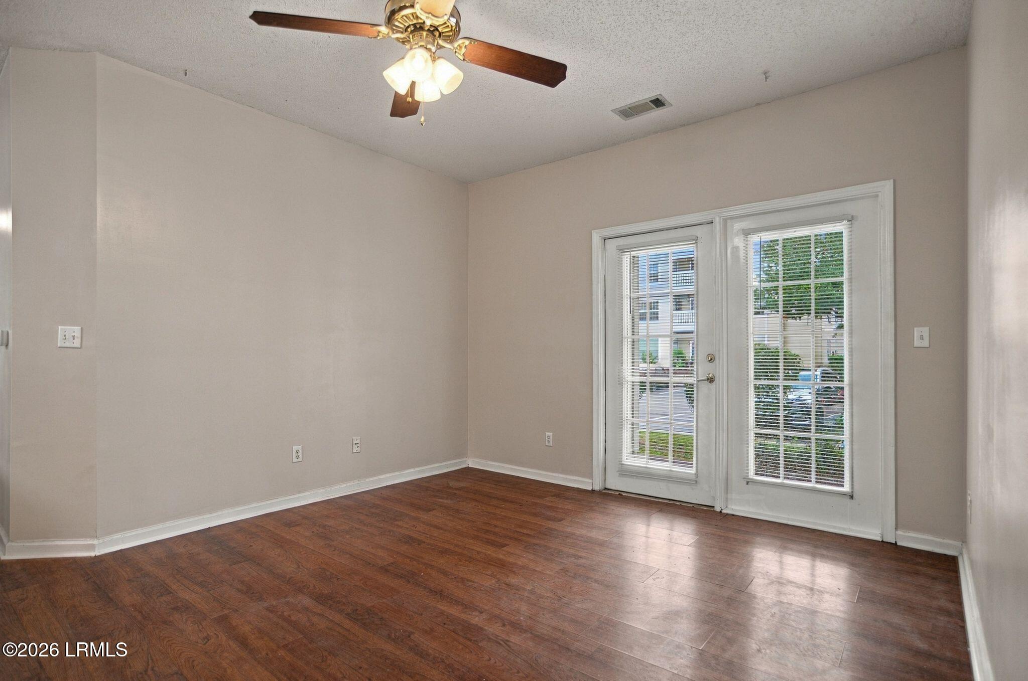 Vacant room with dark hardwood floors, a ceiling fan, and a glazed door with white blinds.