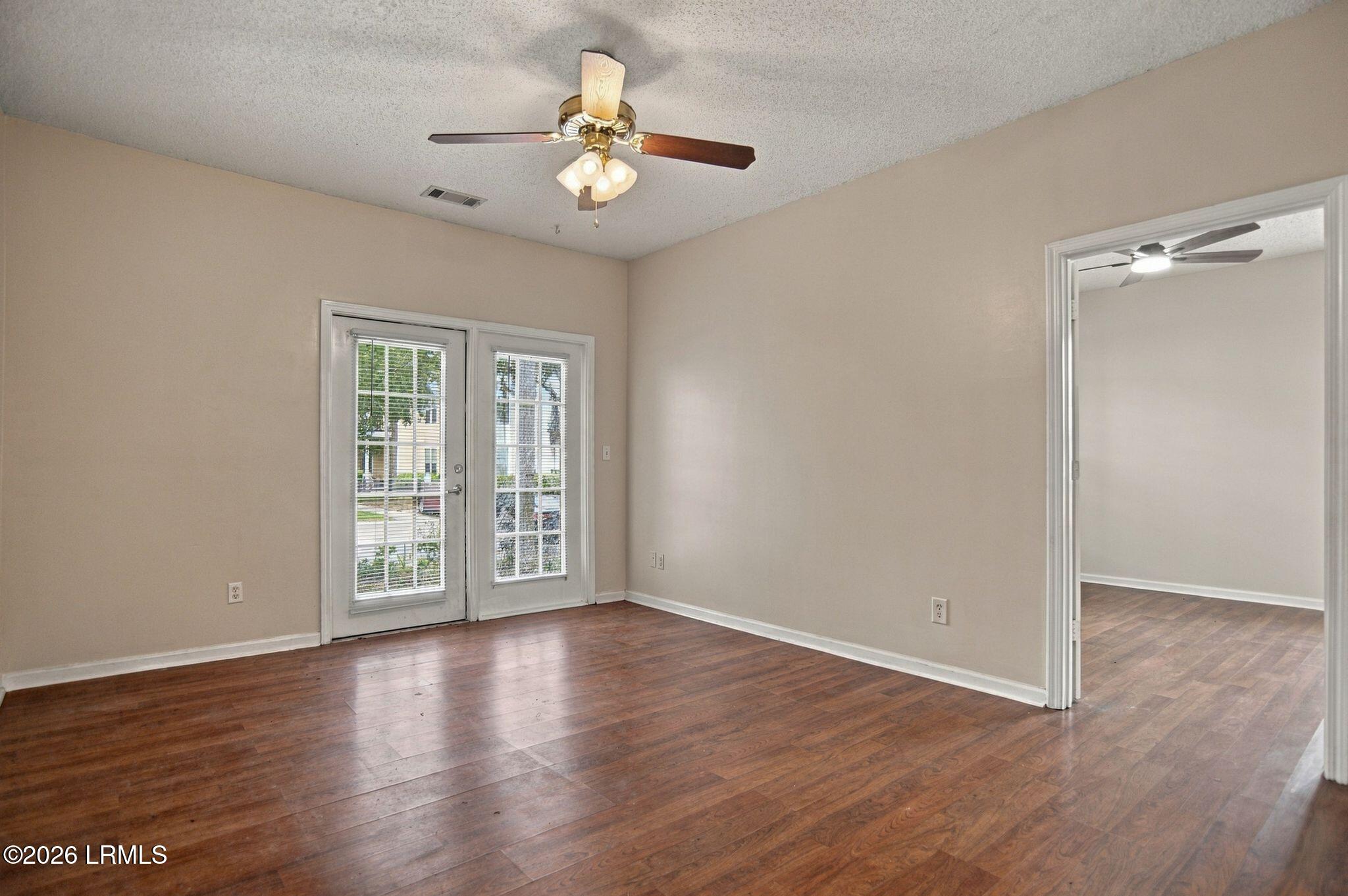 Empty room with hardwood floors, glass-paneled exterior doors, and a wide doorway to another room.