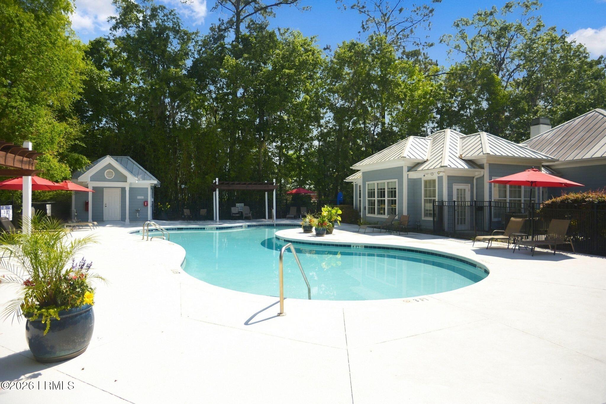 Community swimming pool with a curved shape, red umbrellas, and a blue clubhouse.