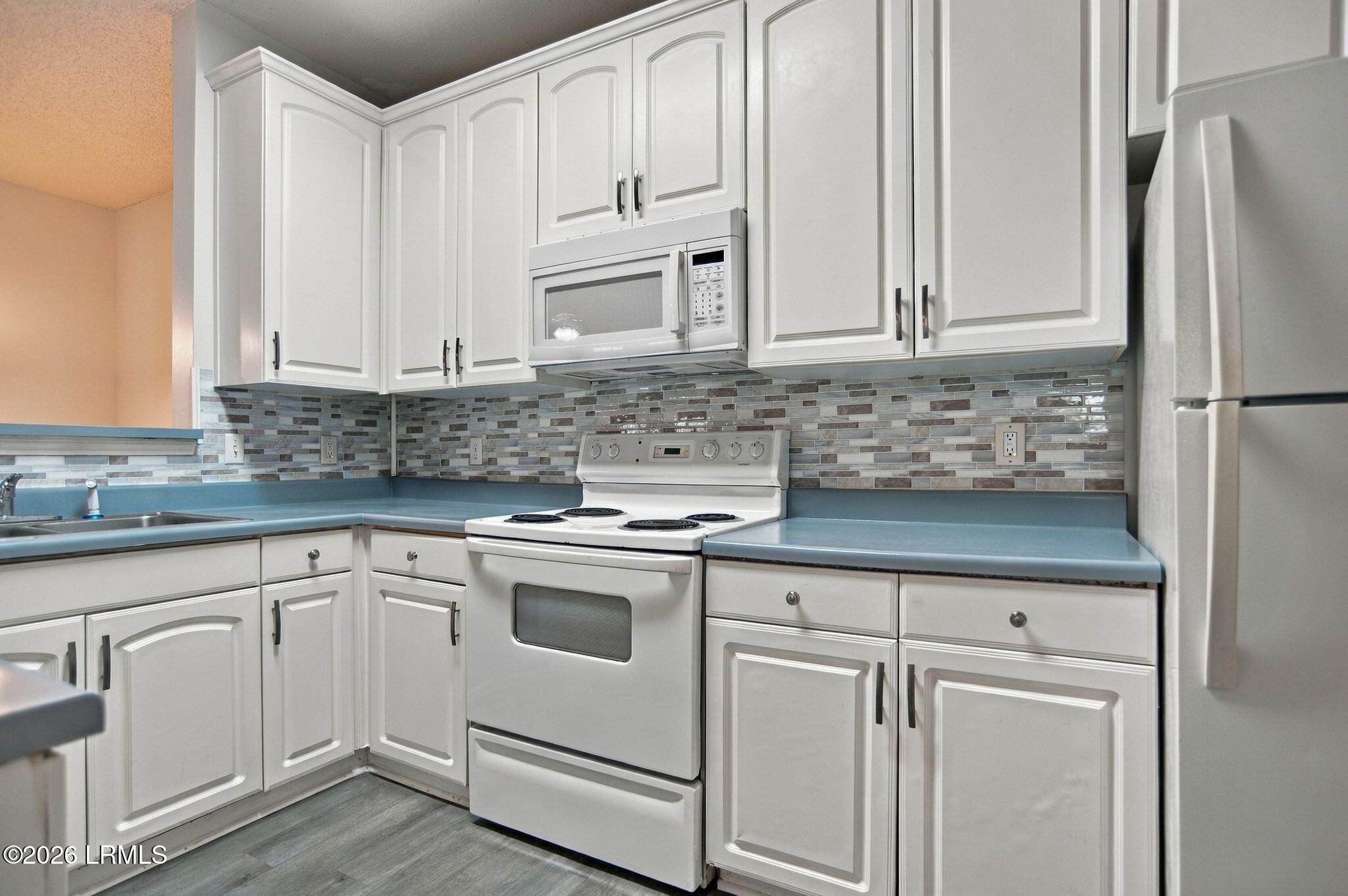 Kitchen with white cabinets, blue countertops, mosaic tile backsplash, and white electric range.