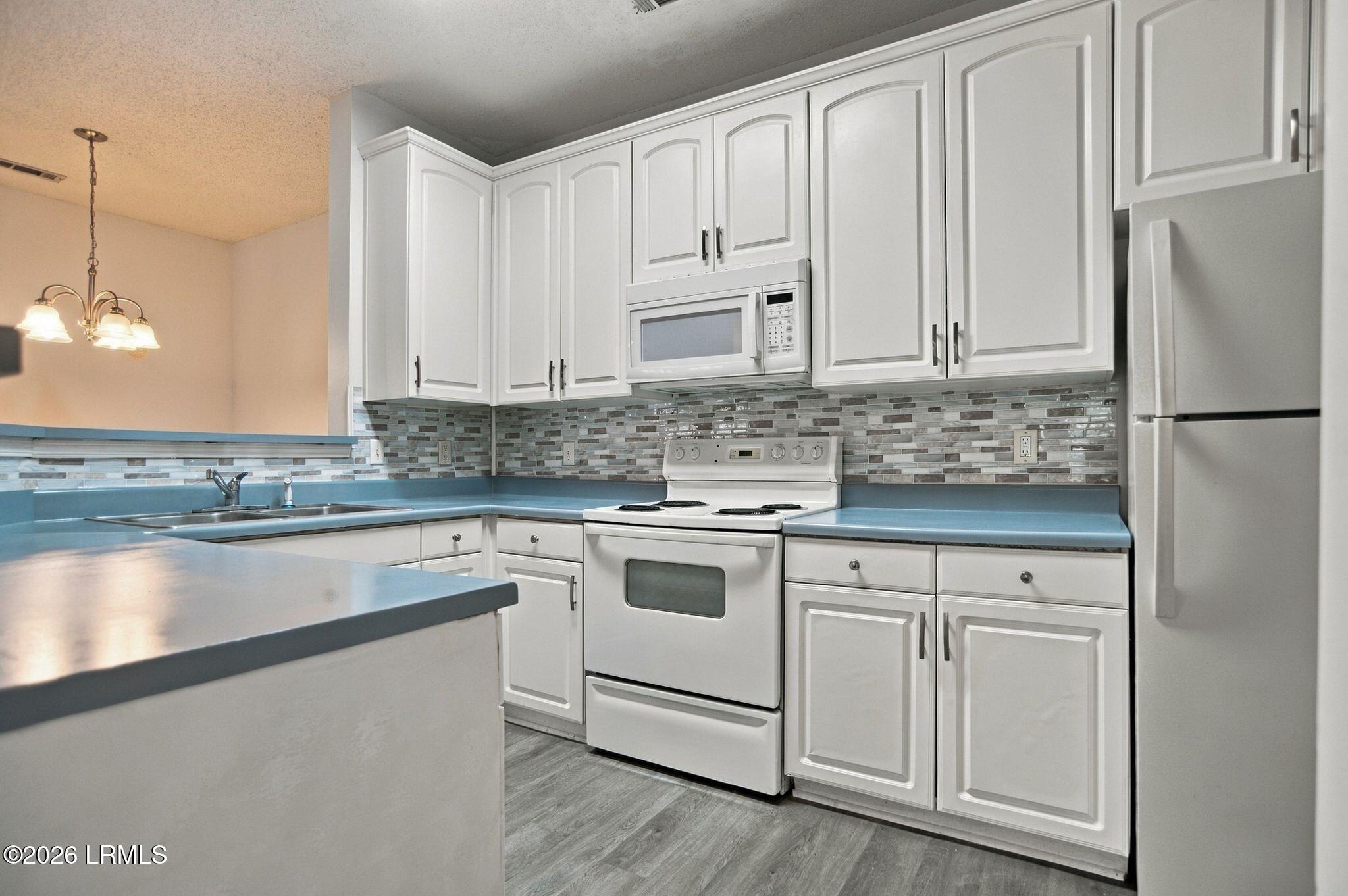 Kitchen with white cabinets, blue countertops, mosaic backsplash, and white appliances.