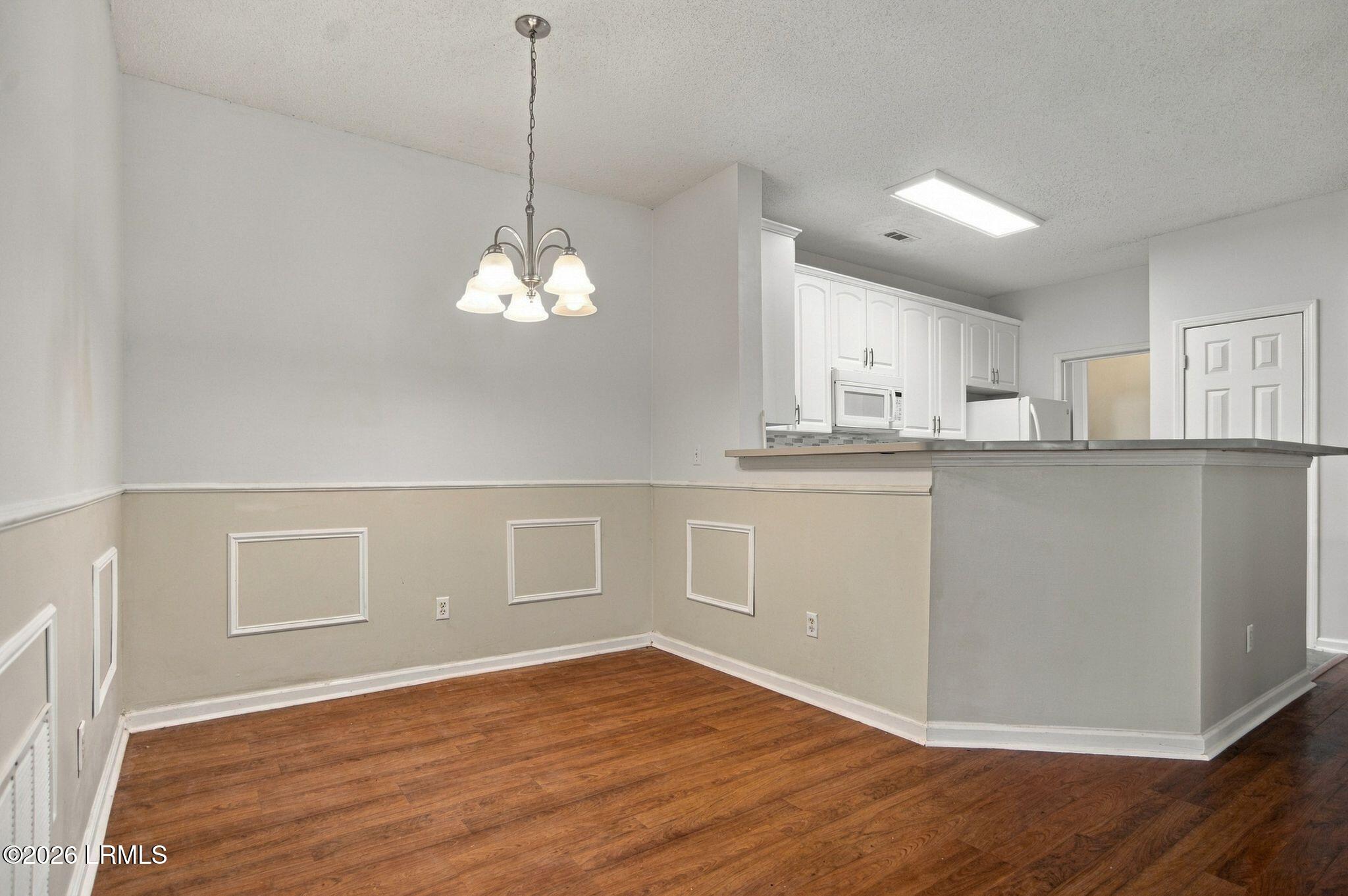 Unfurnished dining area with hardwood floors, decorative wall molding, and a chandelier beside the kitchen.