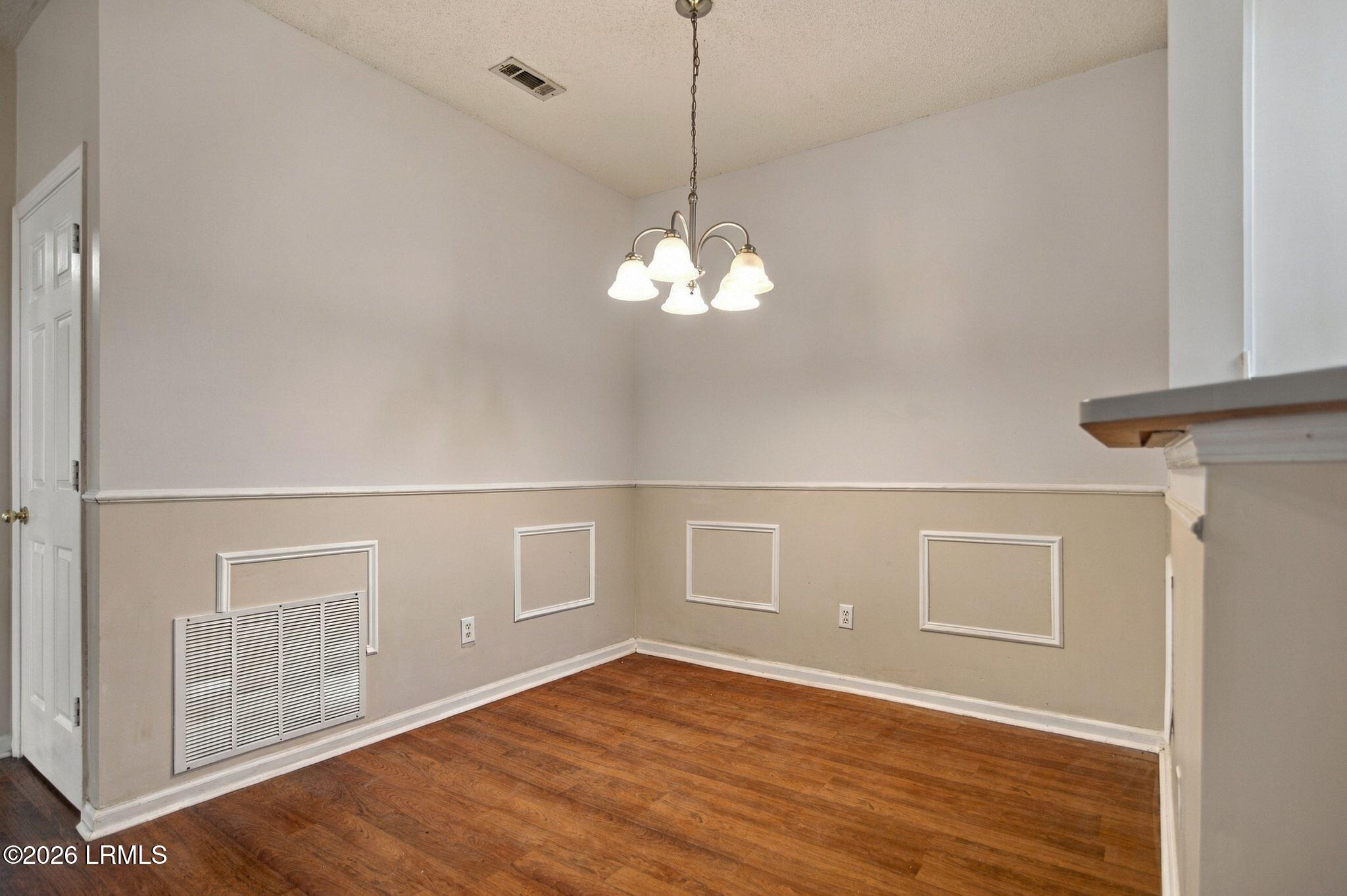Empty dining area with hardwood floors, decorative wall molding, and a hanging chandelier.