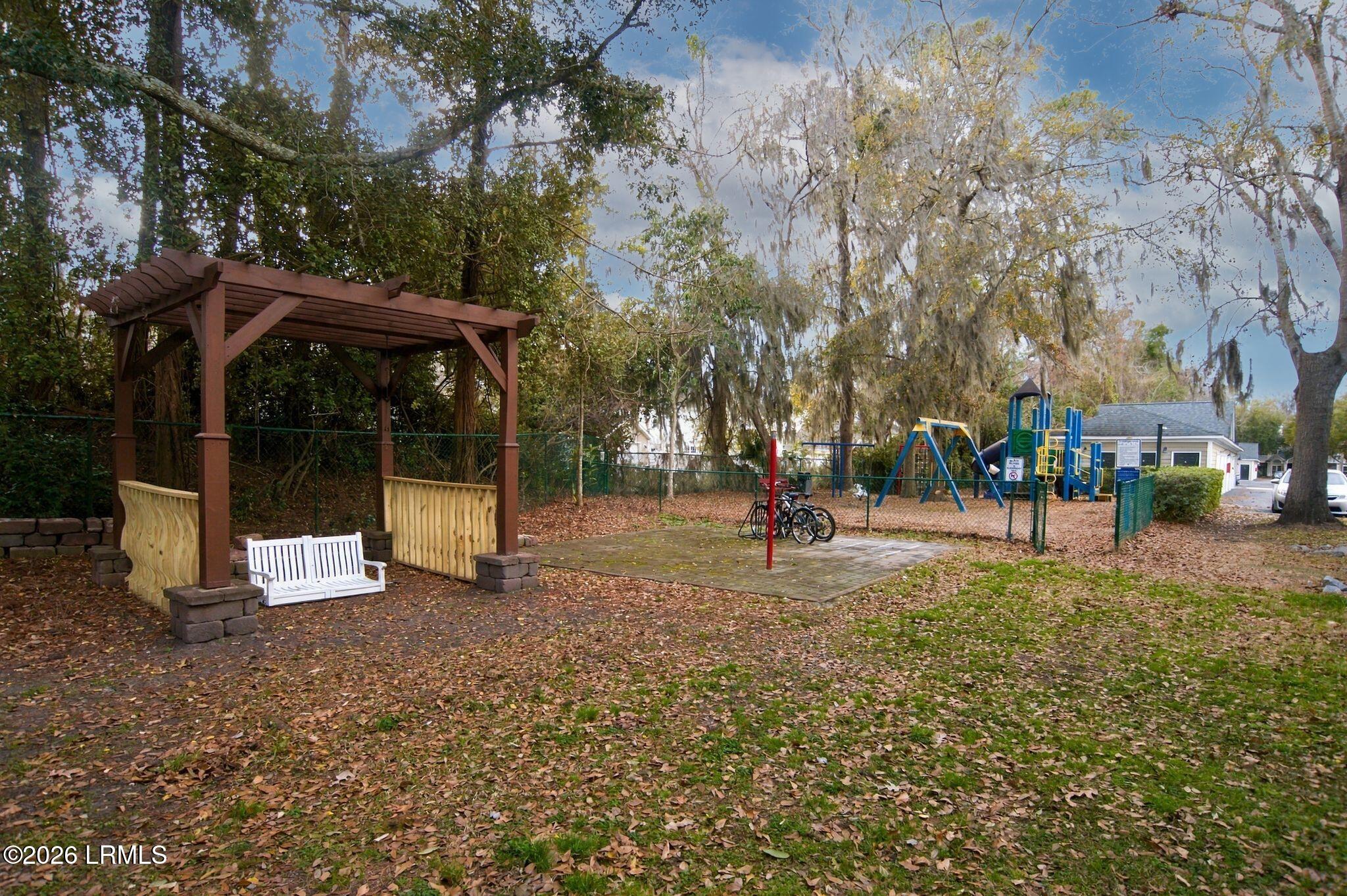 Community playground with swings and climbing equipment beside a wooden pergola and bench.
