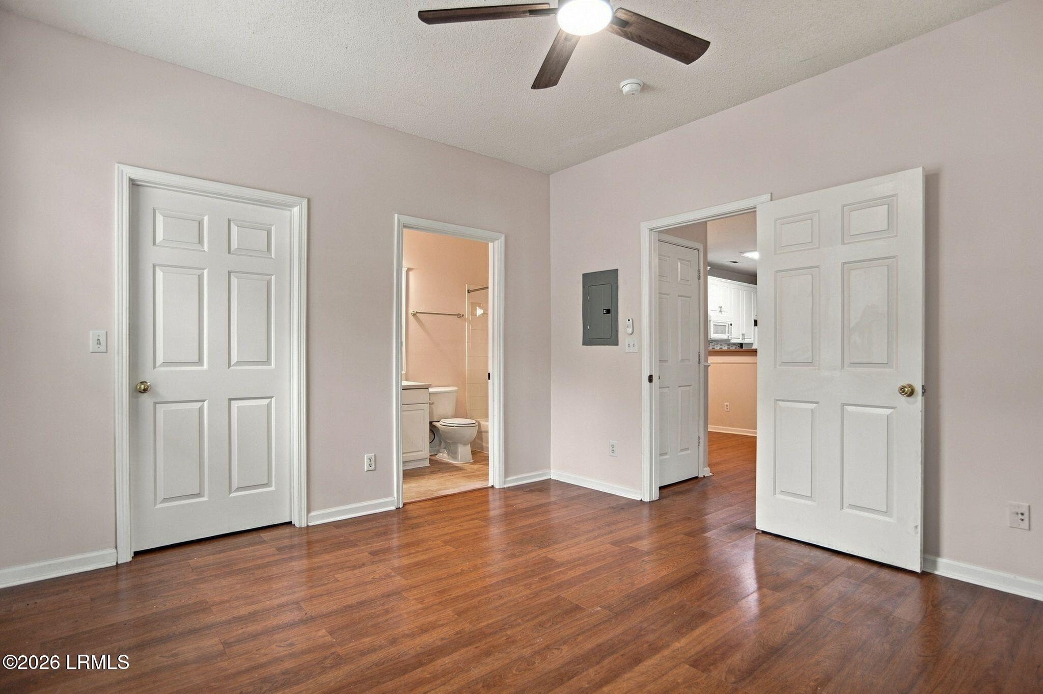 Empty bedroom with hardwood floors and ceiling fan, with an open doorway to the bathroom.
