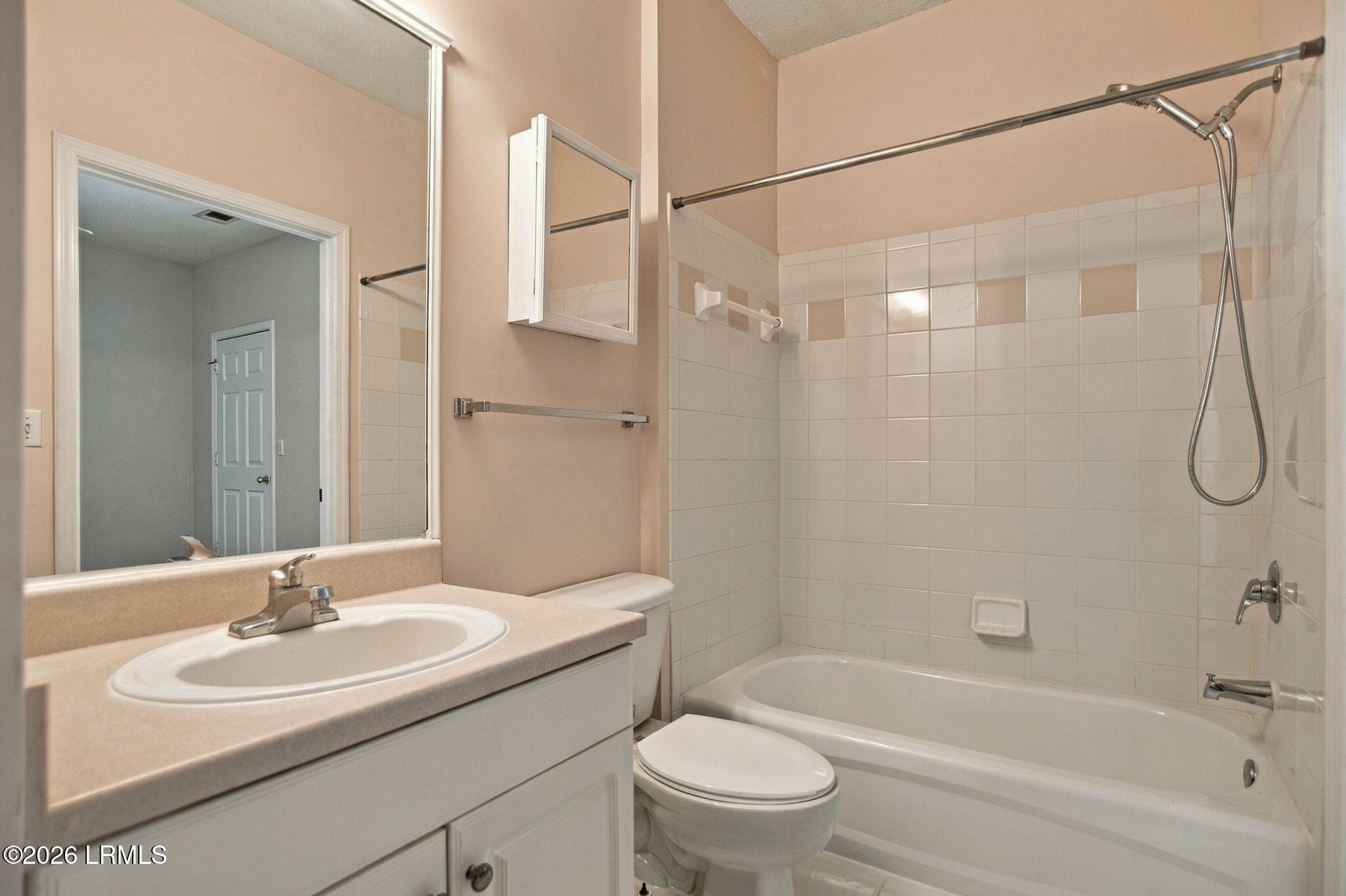 Bathroom with a white vanity, toilet, and tiled tub-shower surround.