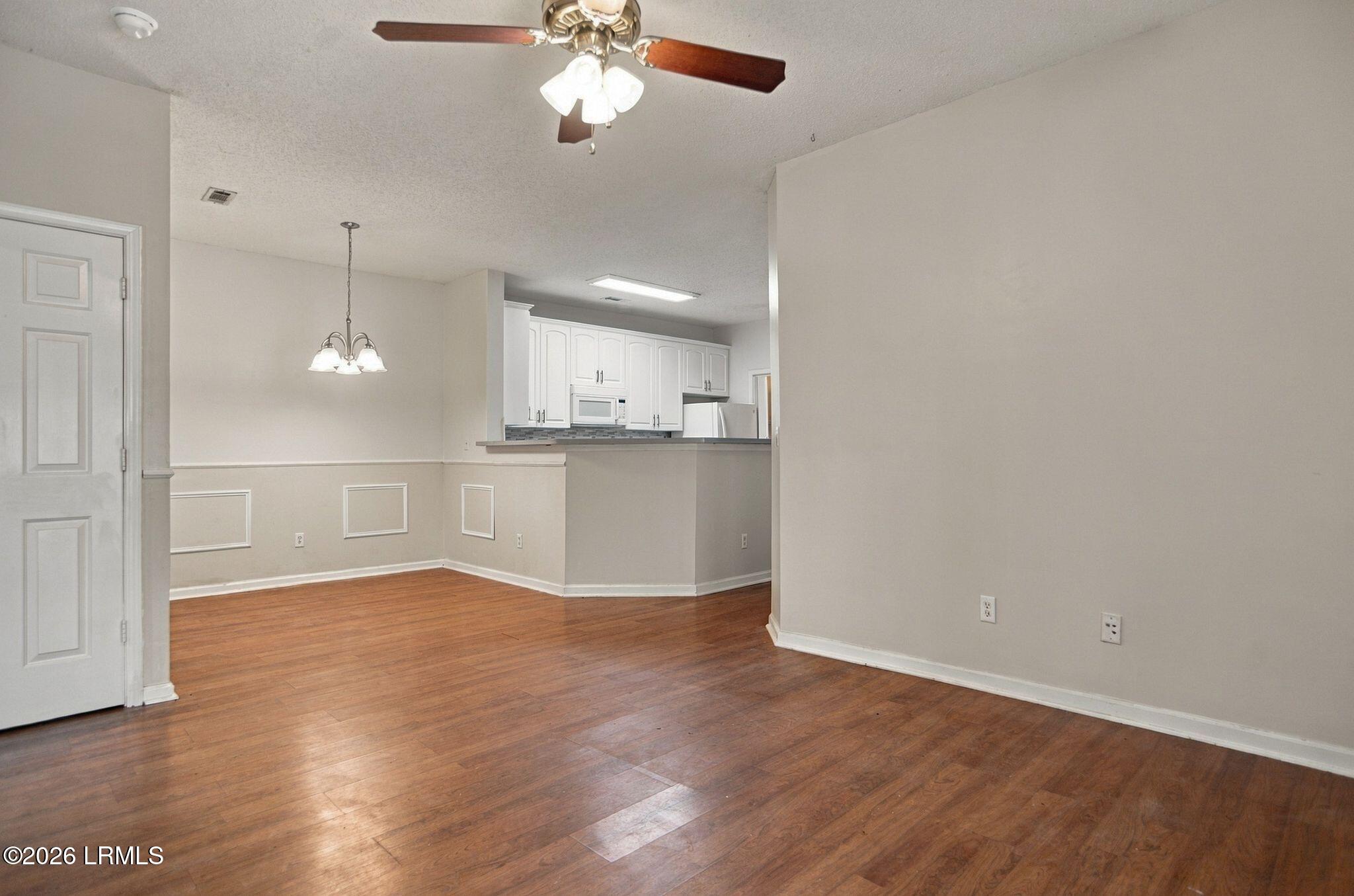 Empty dining area with wood flooring, decorative wall molding, and an opening to the kitchen.