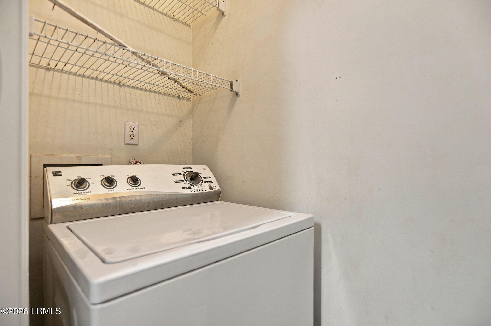 Top-loading washer beneath wire shelves in a laundry closet.