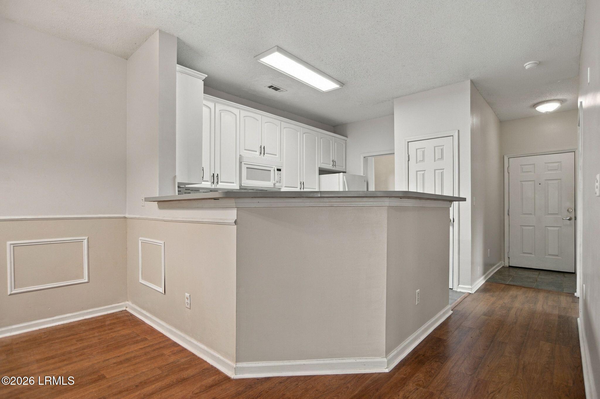 Unfurnished kitchen with white cabinets and a long peninsula counter beside the entry