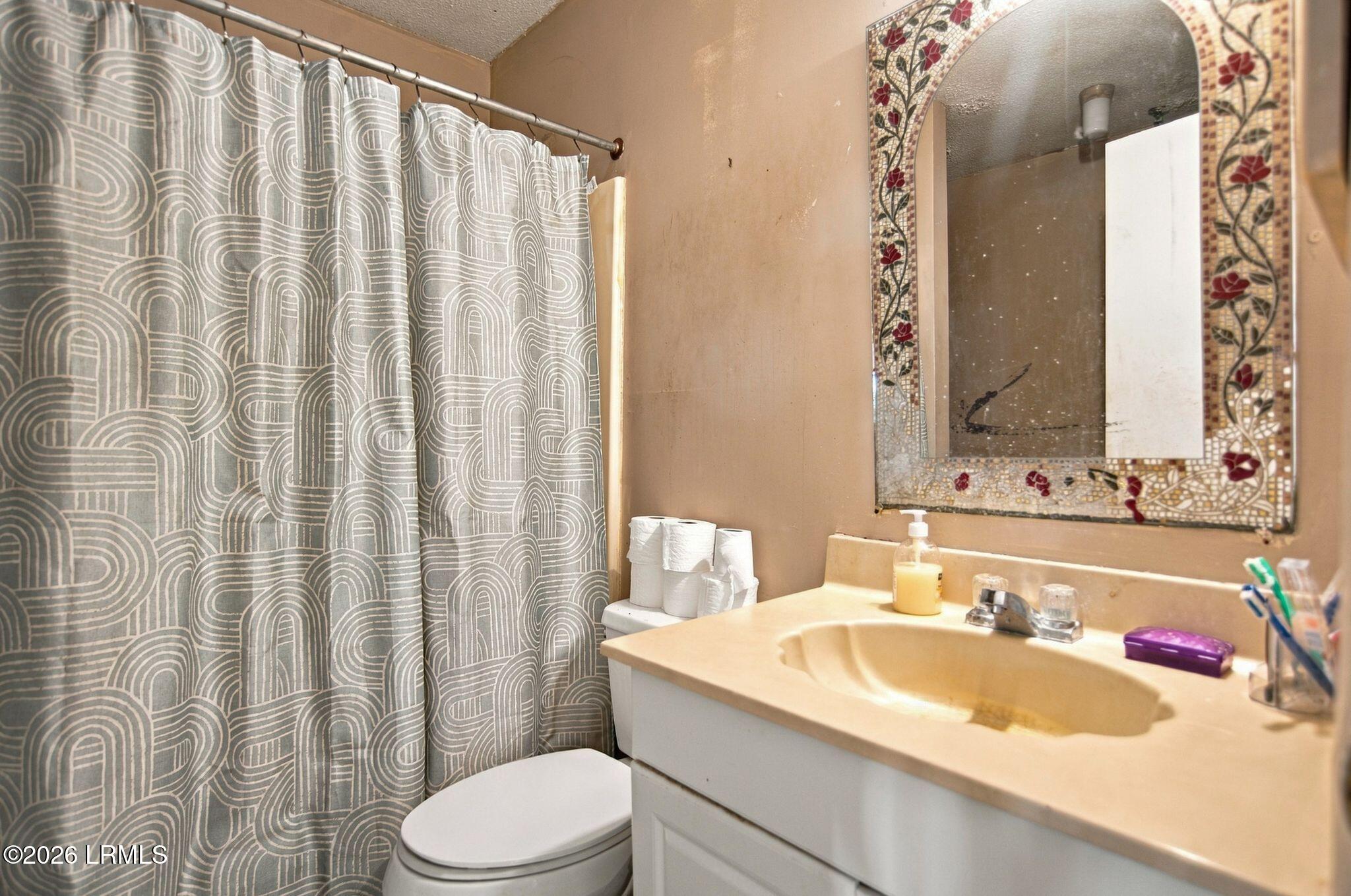 Bathroom with a floral mosaic-framed mirror, patterned shower curtain, and white vanity.