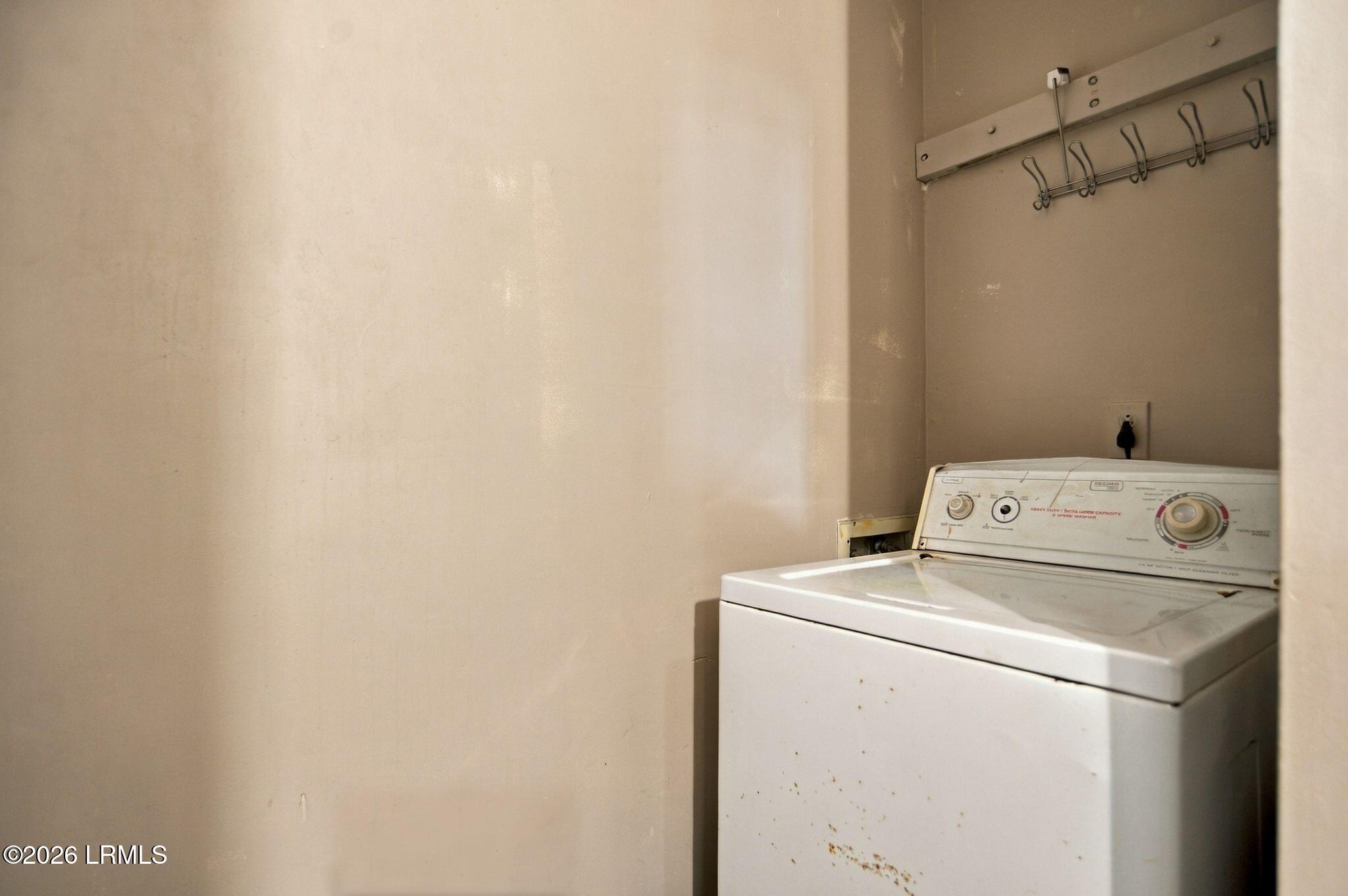 Laundry area with a white top-loading washer and wall-mounted hooks.