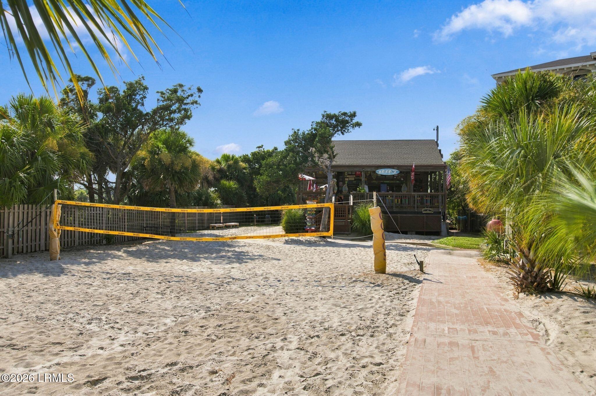 Sandy volleyball court beside a palm-lined pavilion and brick walkway.