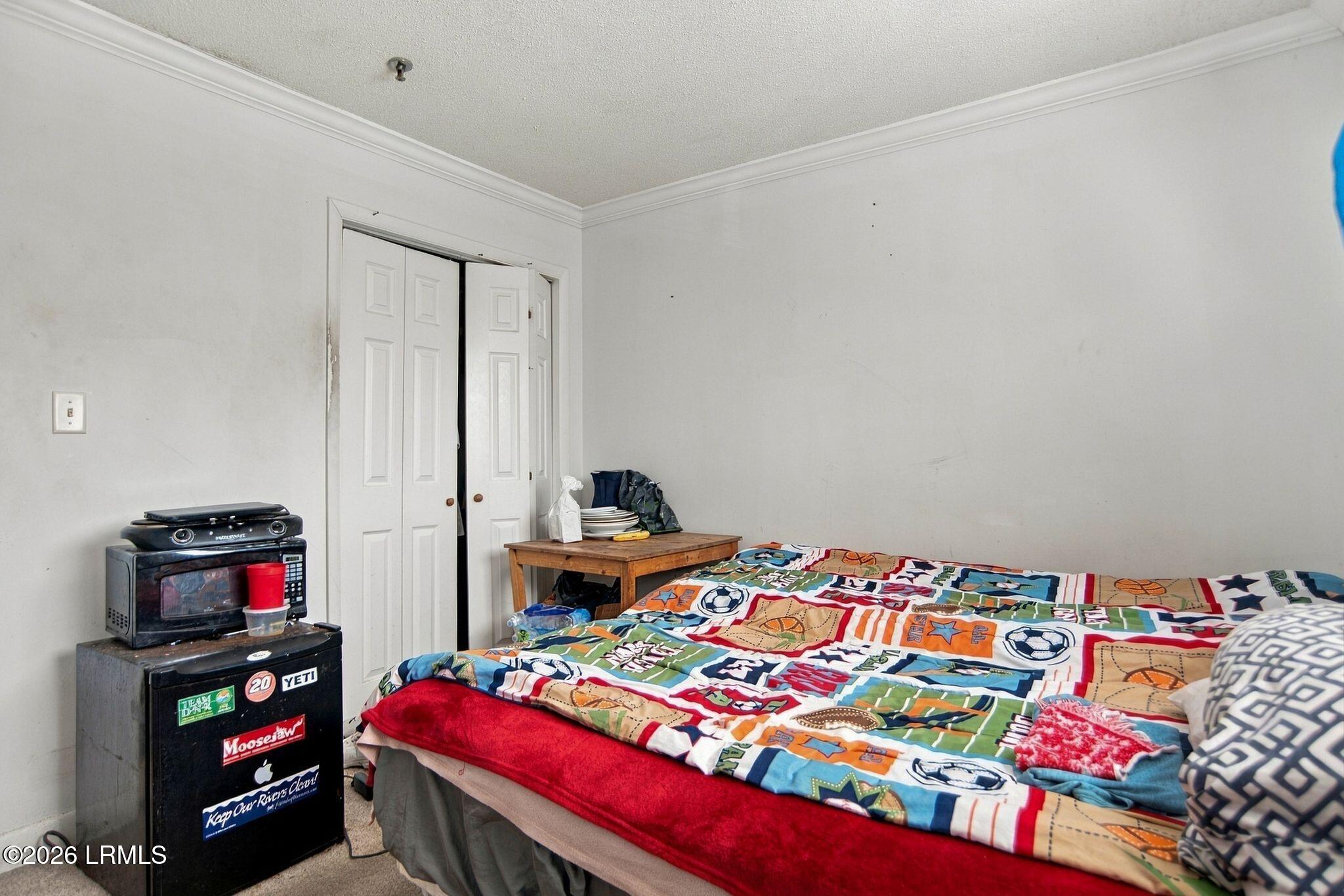 Bedroom with a colorful sports-pattern bedspread, closet doors, and a microwave atop a compact refrigerator.